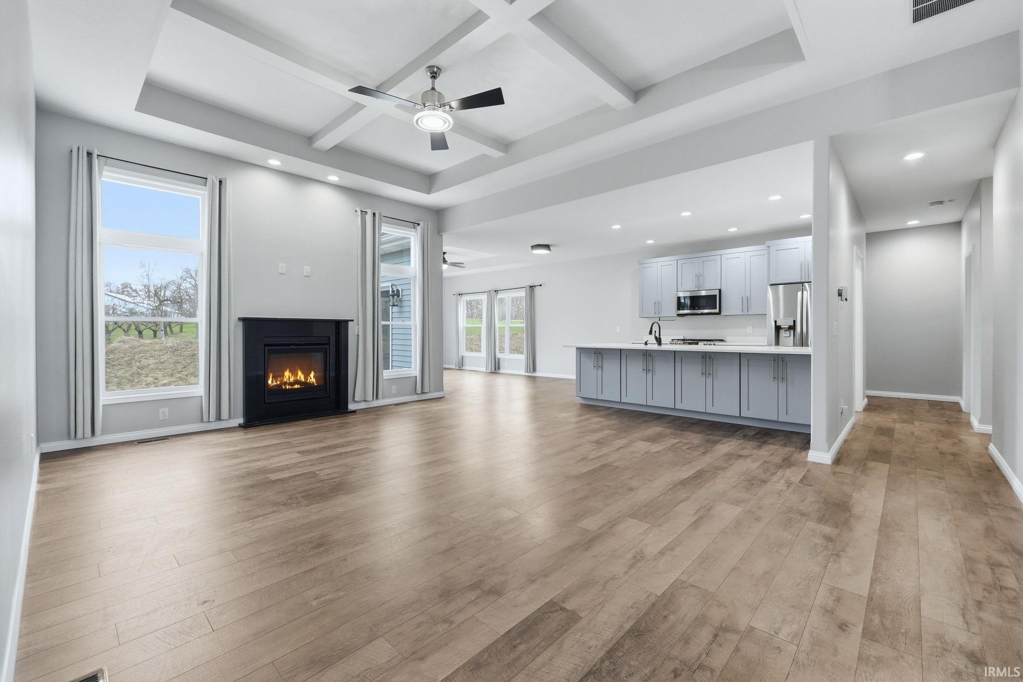 Unfurnished living room with coffered ceiling, a glass covered fireplace, a ceiling fan, recessed lighting, and light wood-style flooring