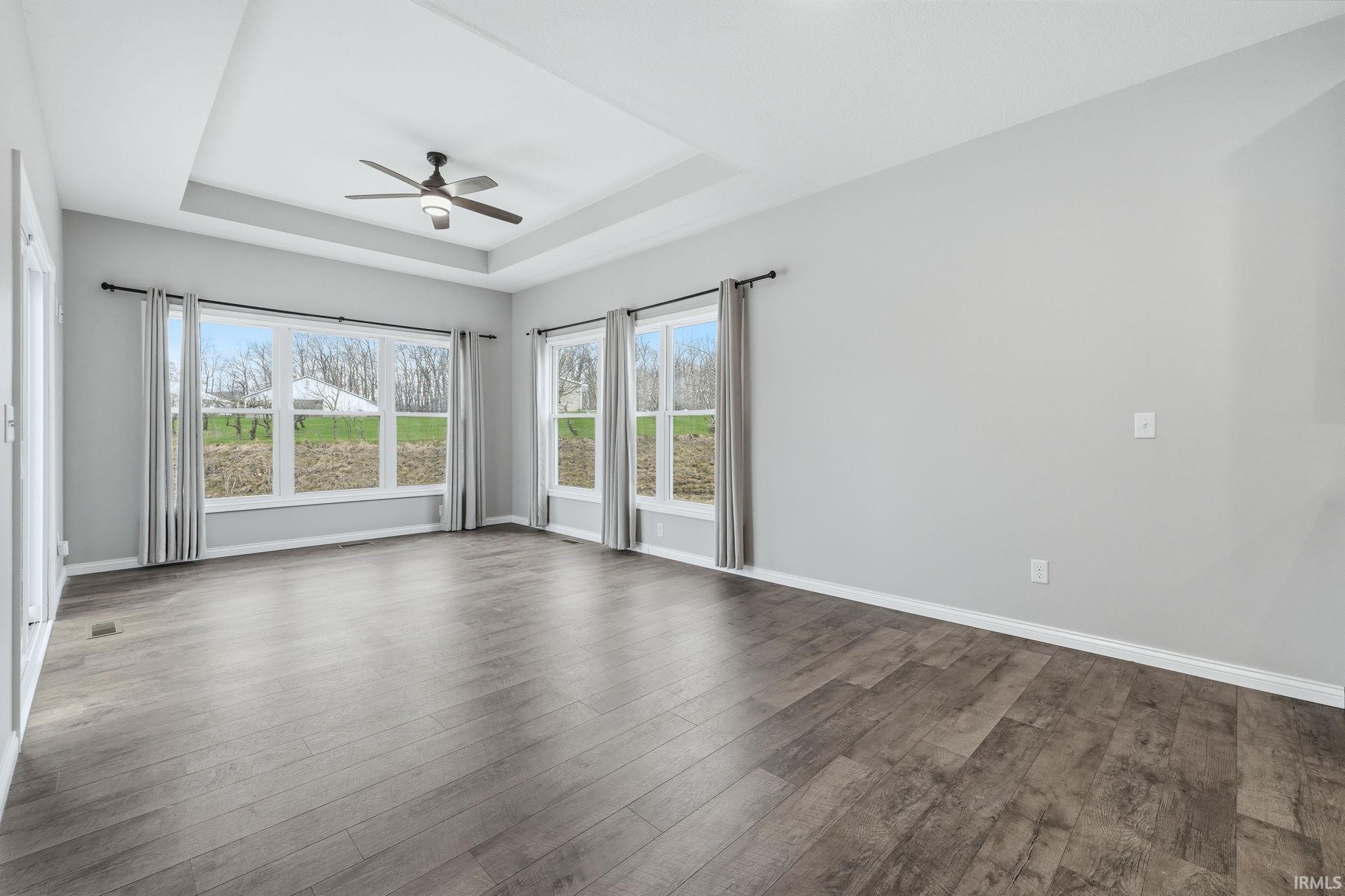 Unfurnished room featuring a ceiling fan, dark wood finished floors, and a raised ceiling