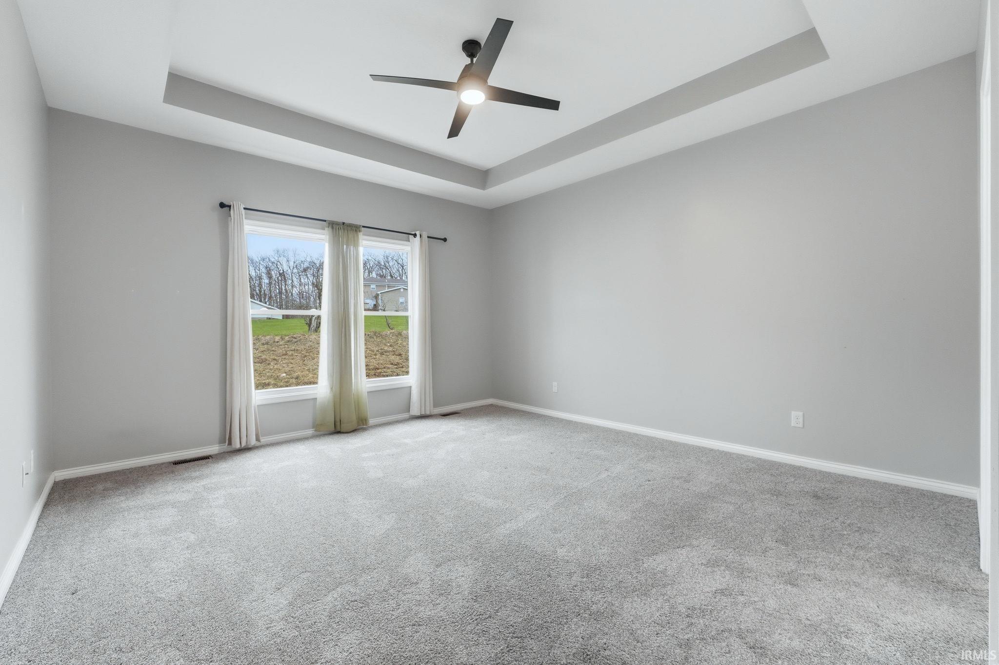 Spare room with a raised ceiling, light carpet, and a ceiling fan