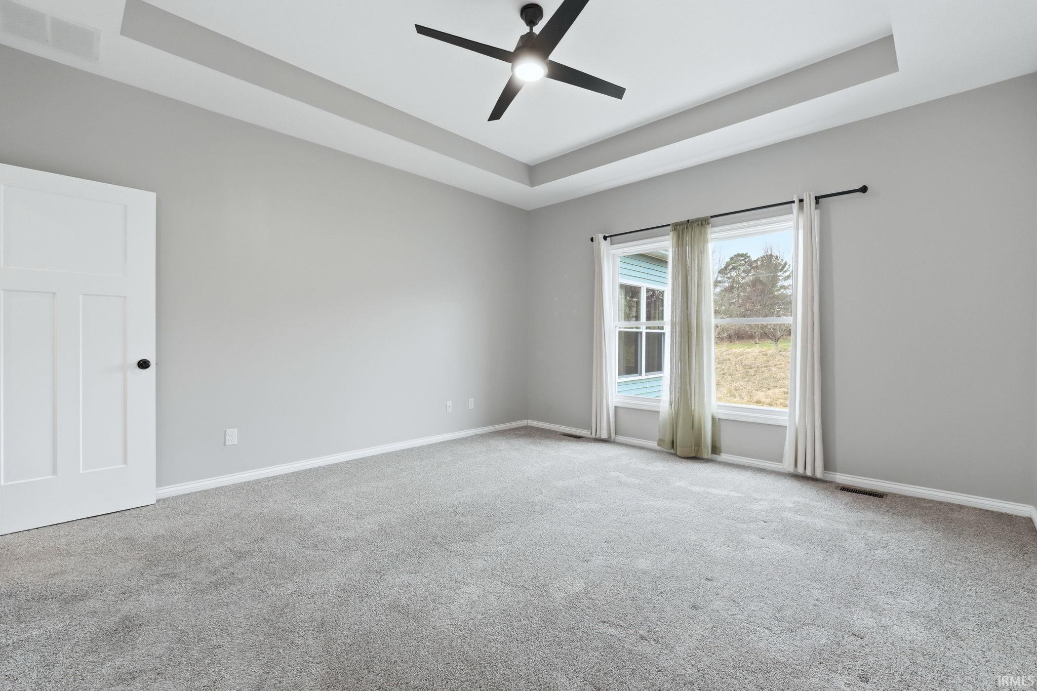 Empty room featuring a raised ceiling, ceiling fan, and light colored carpet