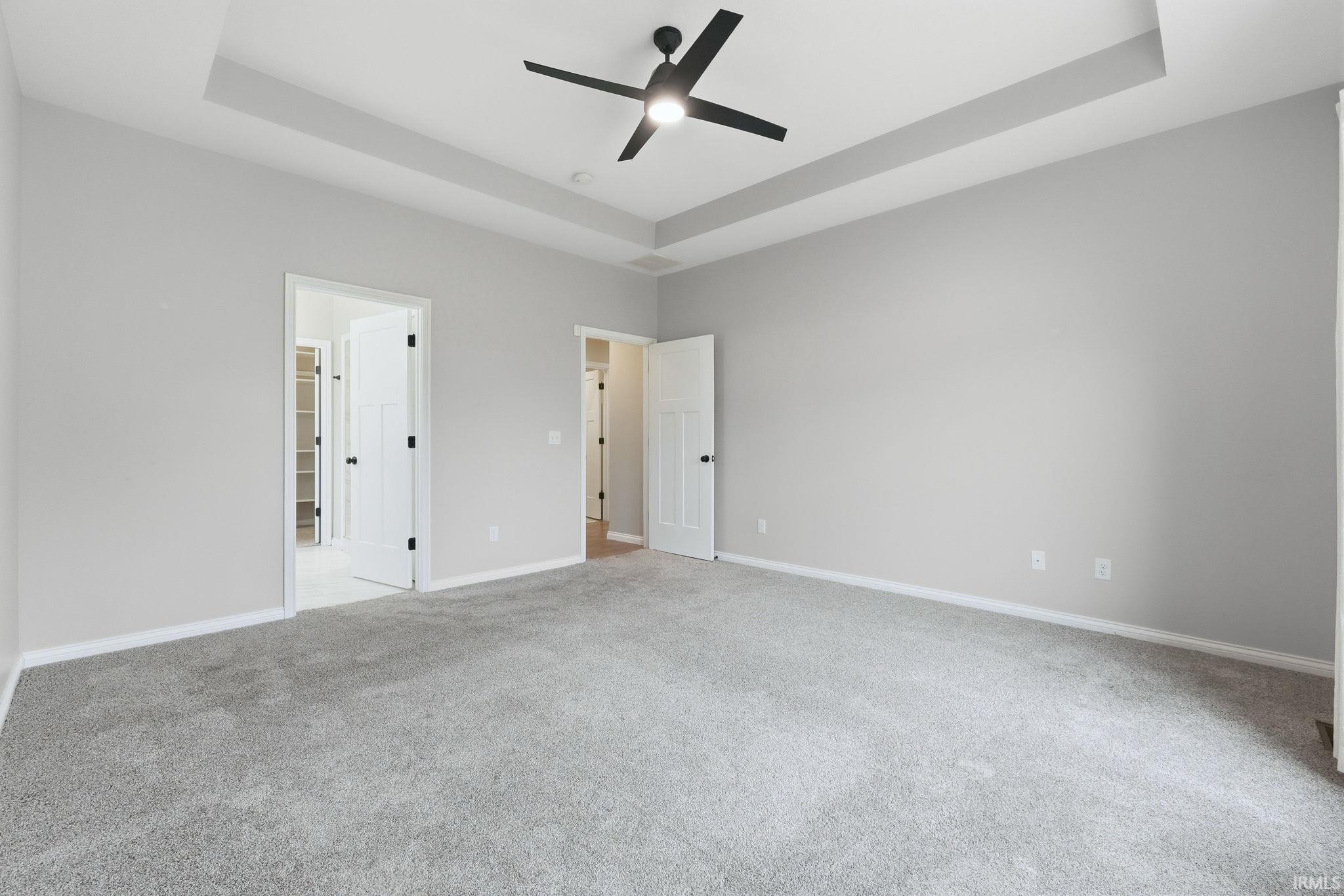 Unfurnished bedroom with a raised ceiling, light colored carpet, and a ceiling fan