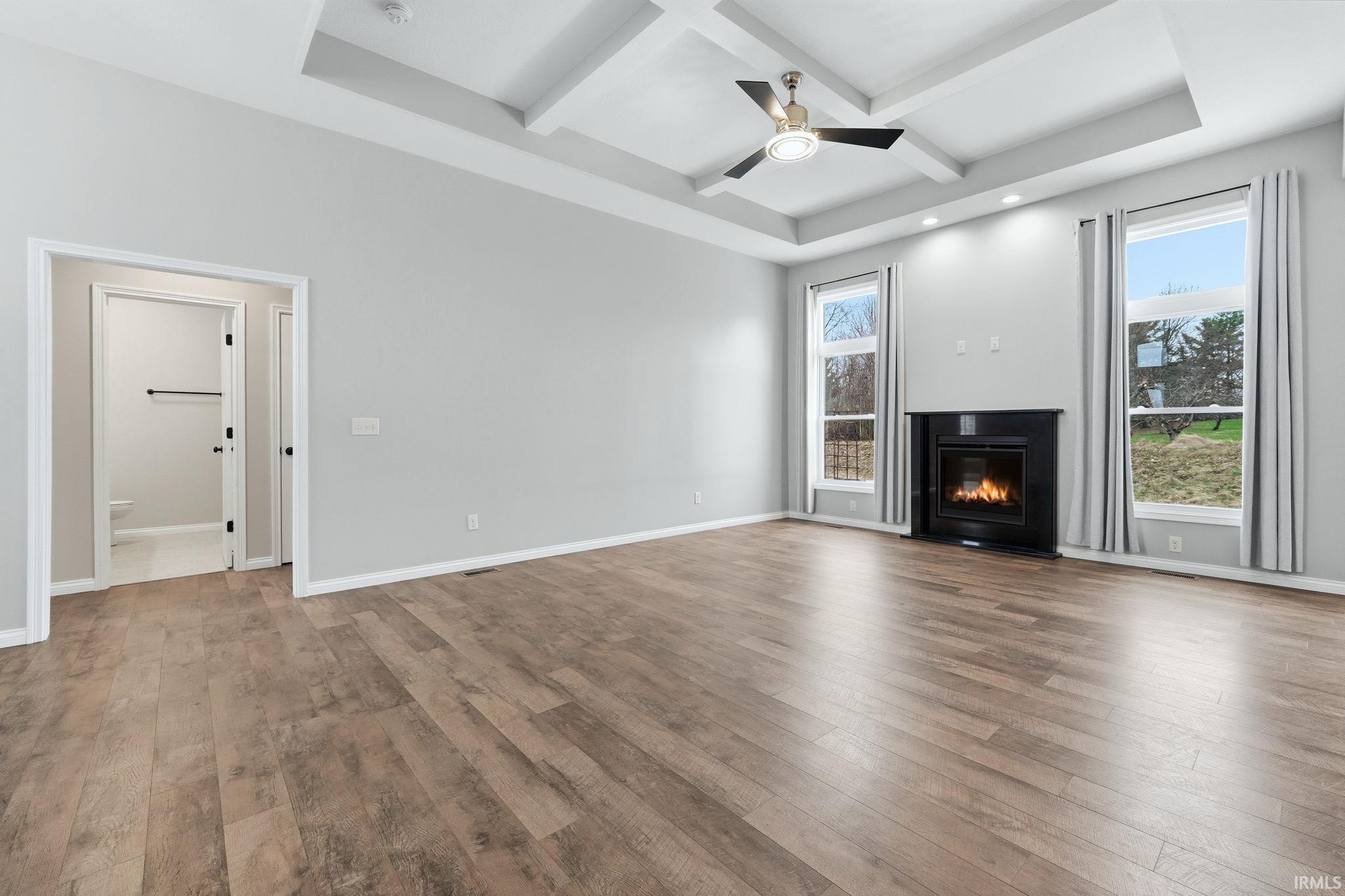 Unfurnished living room featuring coffered ceiling, a ceiling fan, a glass covered fireplace, and dark wood-style flooring