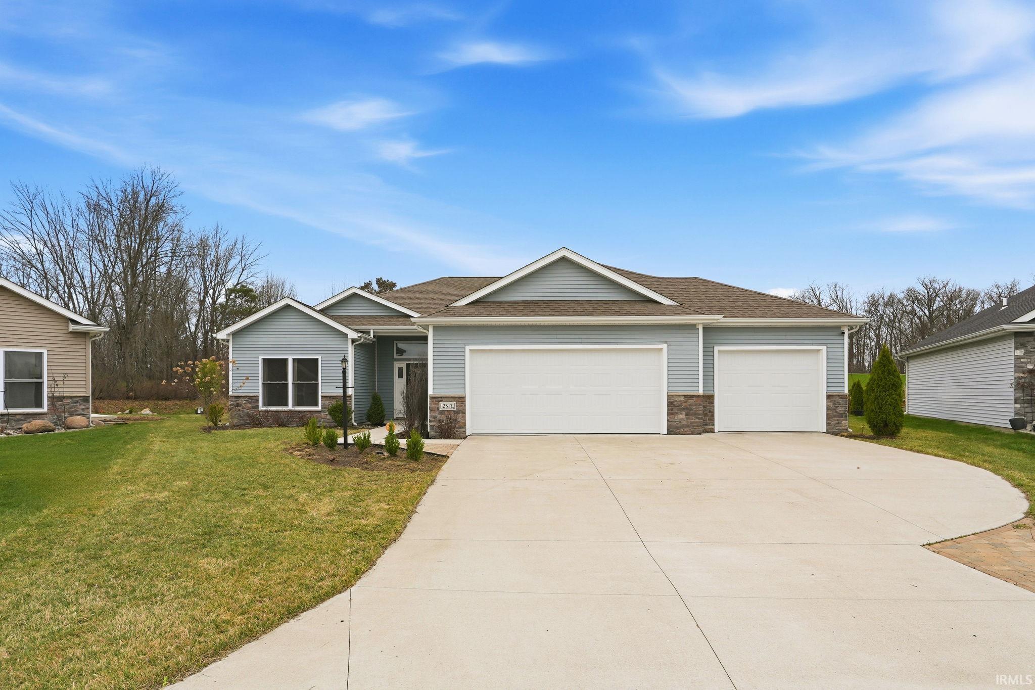 View of front of home with a front lawn, stone siding, a garage, and concrete driveway