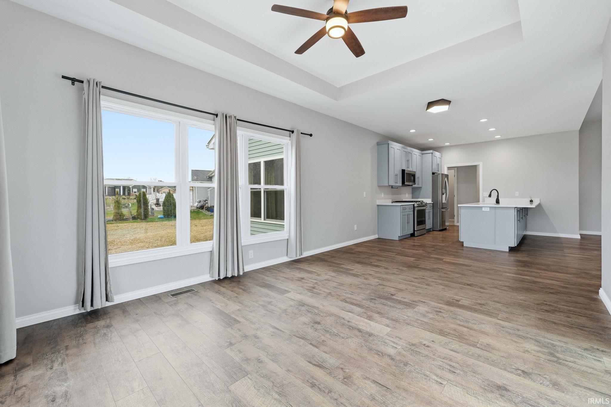 Unfurnished living room with ceiling fan, a tray ceiling, light wood-style flooring, and recessed lighting