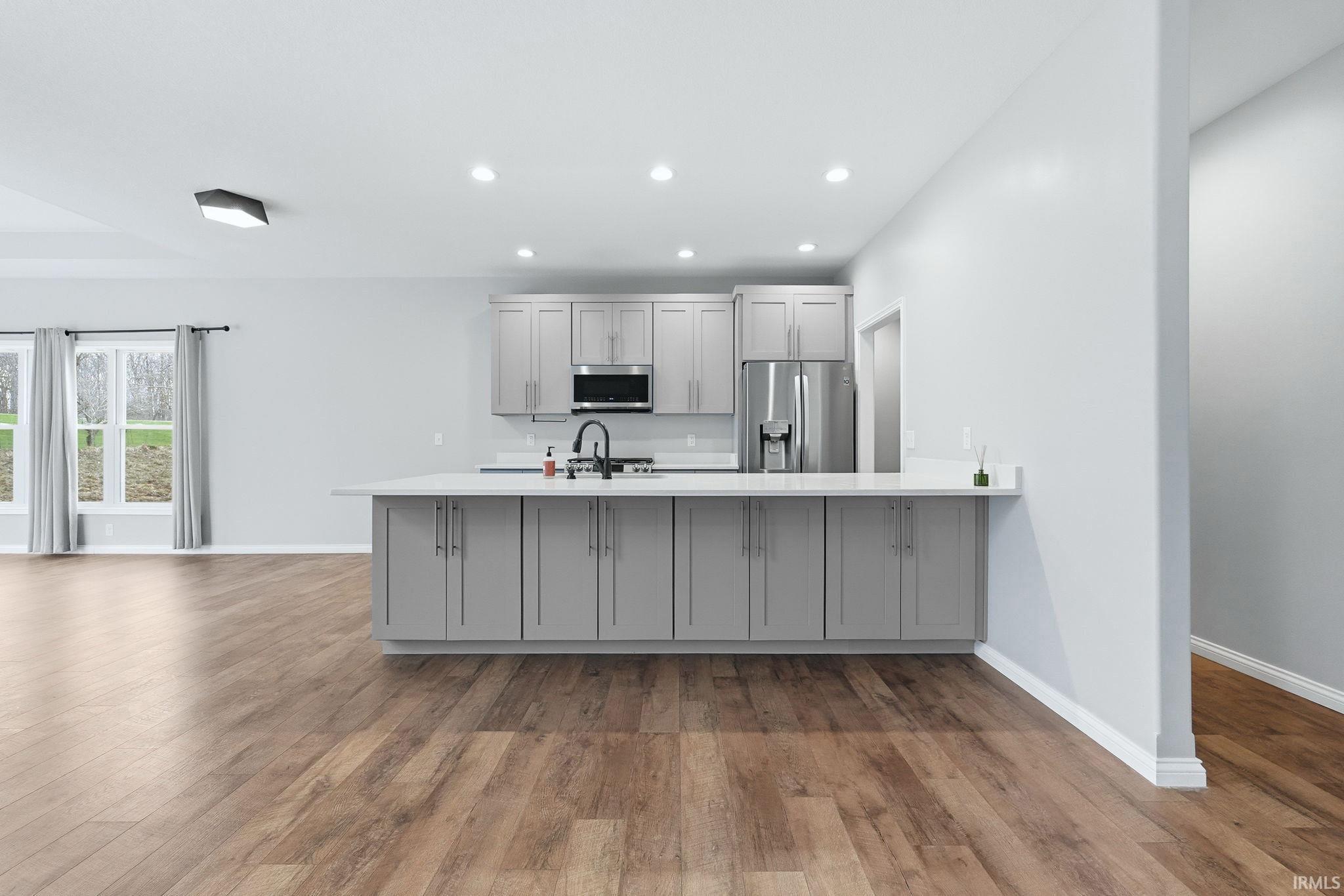 Open-concept kitchen featuring light gray cabinetry, white countertops, recessed lighting, and stainless steel appliances