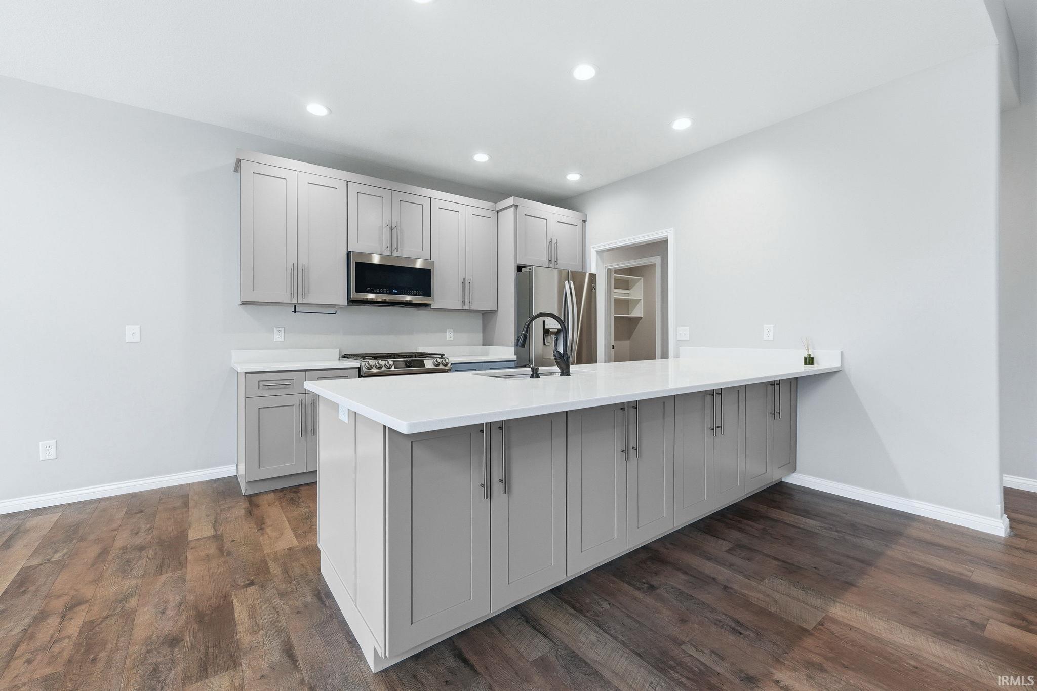 Modern kitchen featuring light gray cabinetry, white countertops, stainless steel appliances, and wood-finish flooring