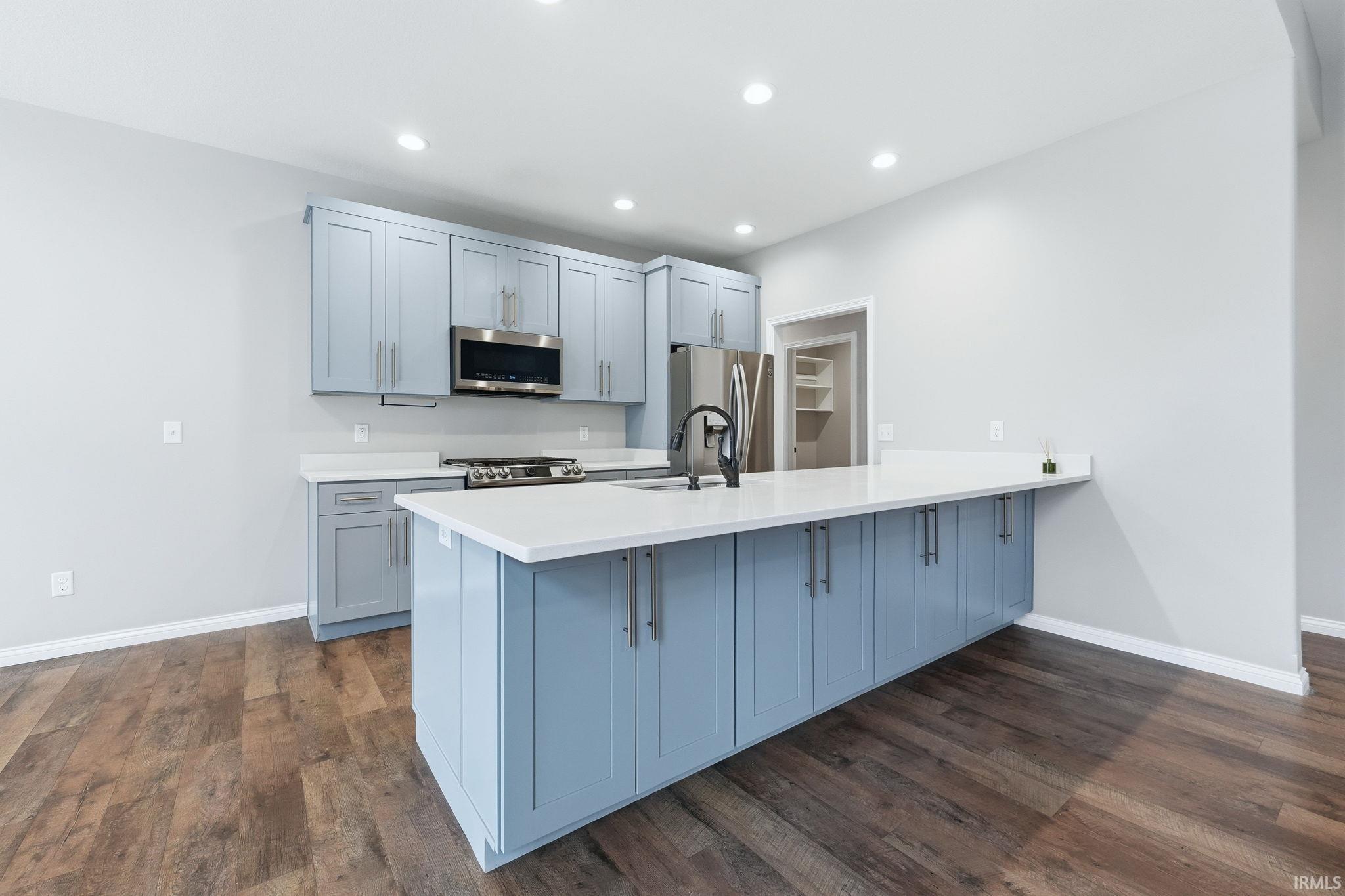 Kitchen with a peninsula, stainless steel appliances, dark wood-style flooring, light stone countertops, and recessed lighting