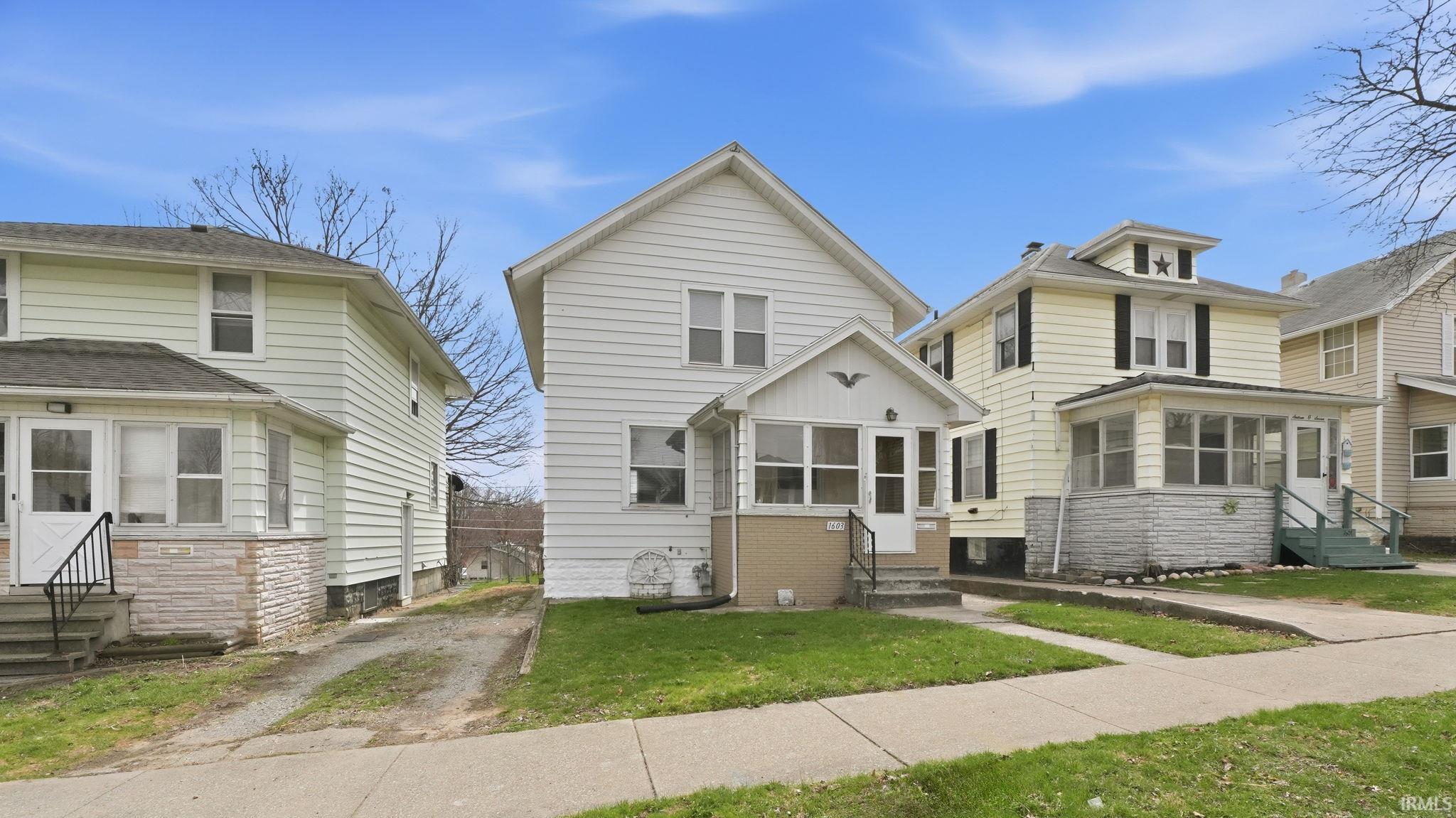 American foursquare style home with entry steps, a sunroom, and a front lawn
