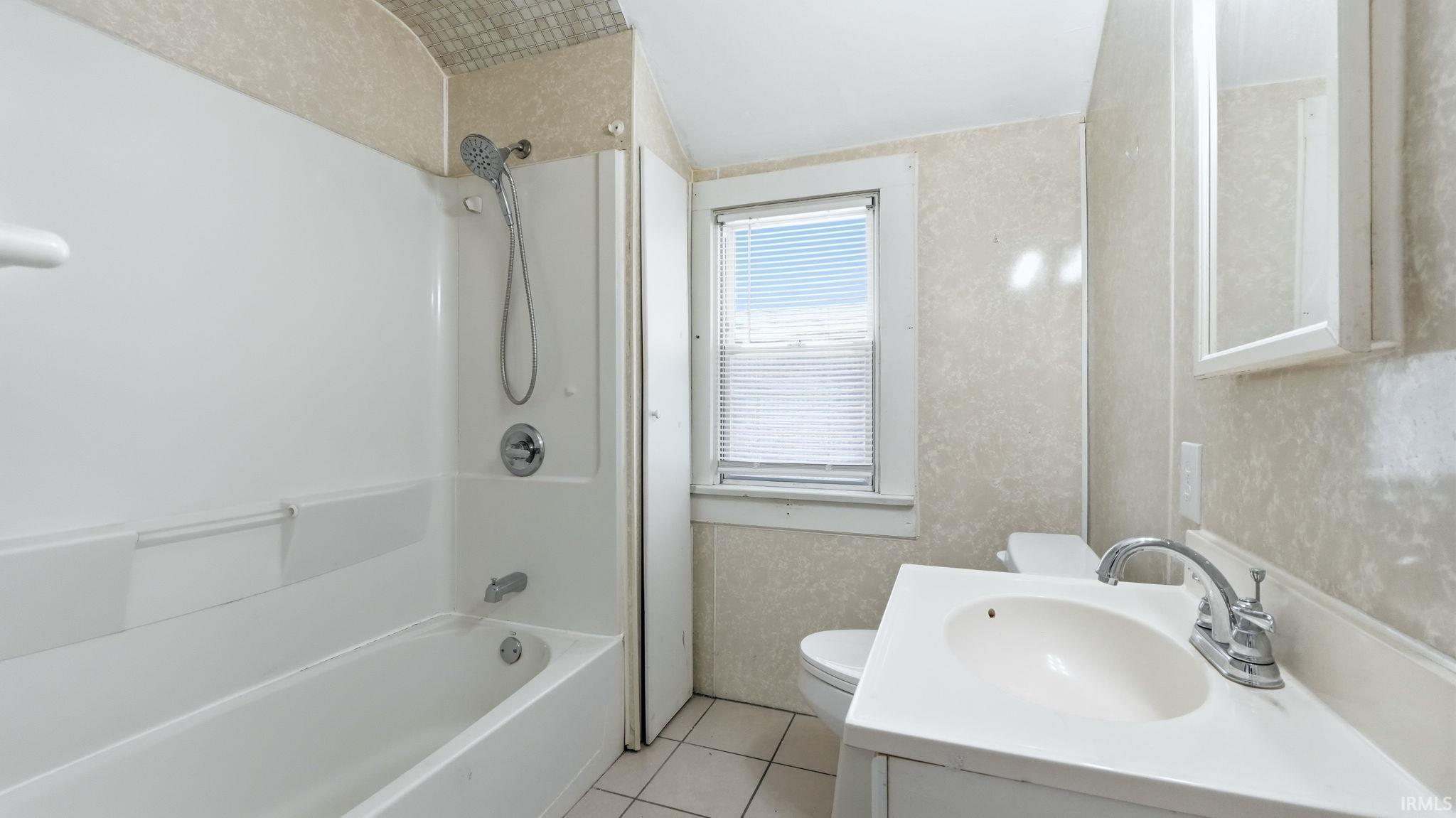 Full bath featuring vanity, tub / shower combination, light tile patterned floors, and wallpapered walls