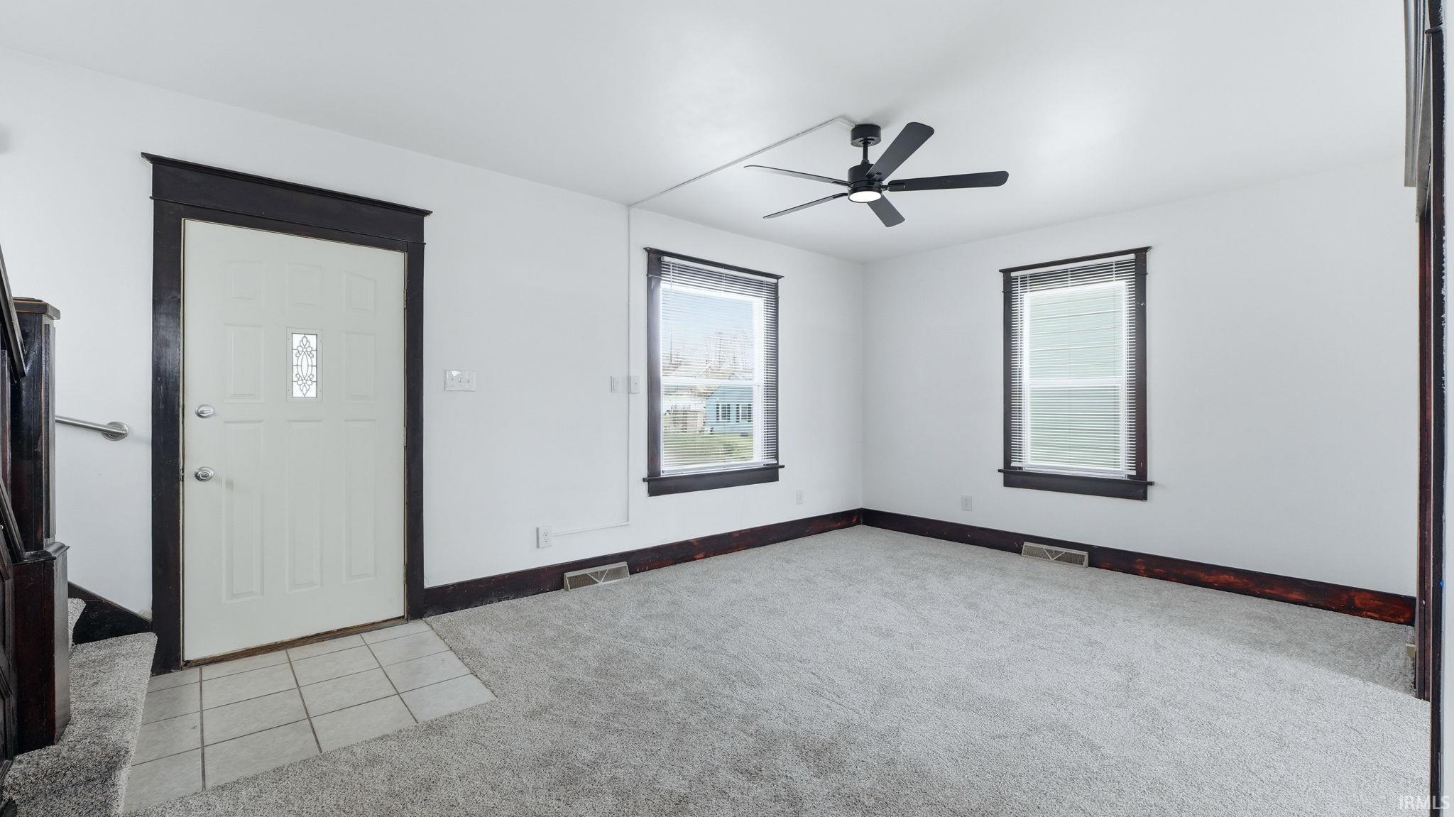 Empty room featuring light carpet, a ceiling fan, and light tile patterned floors