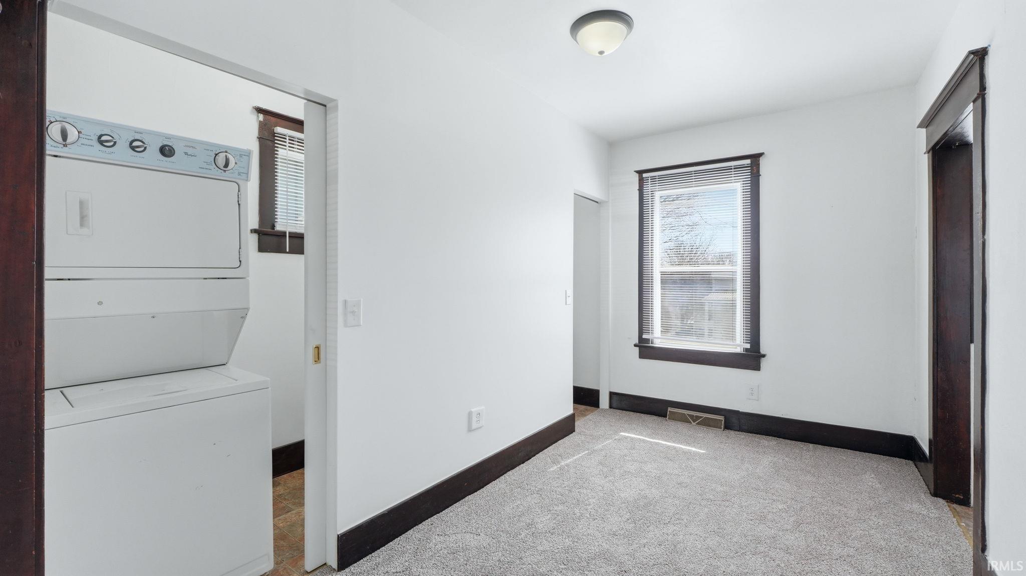 Laundry area with stacked washing machine and dryer and carpet