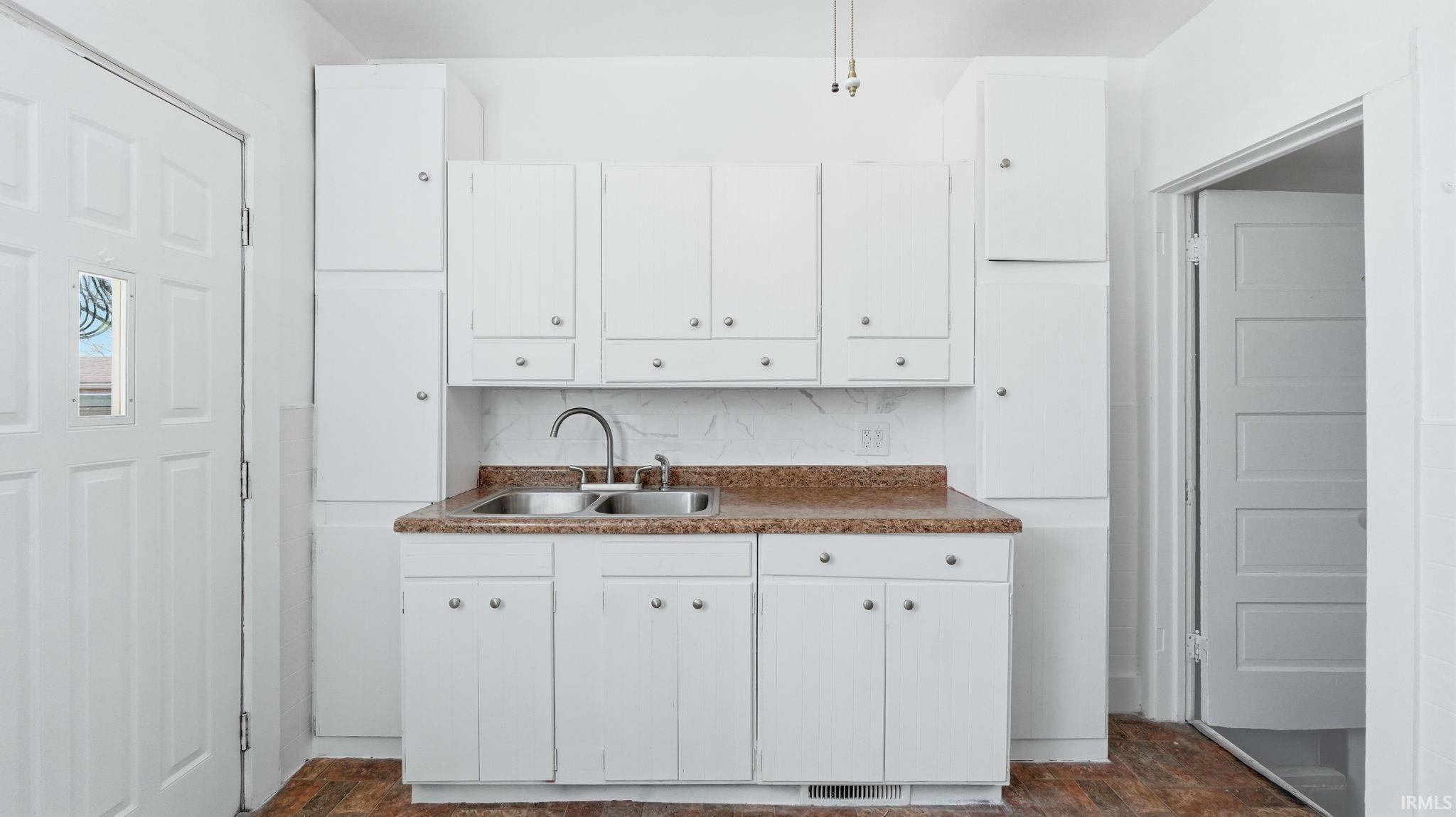 Kitchen featuring white cabinetry, dark countertops, backsplash, and stone finish floors