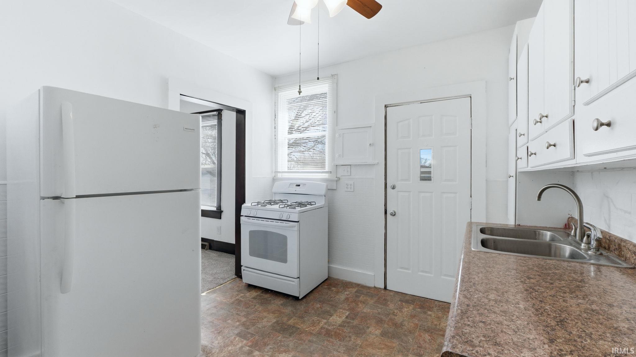 Kitchen featuring white appliances, white cabinets, stone finish floors, ceiling fan, and dark countertops