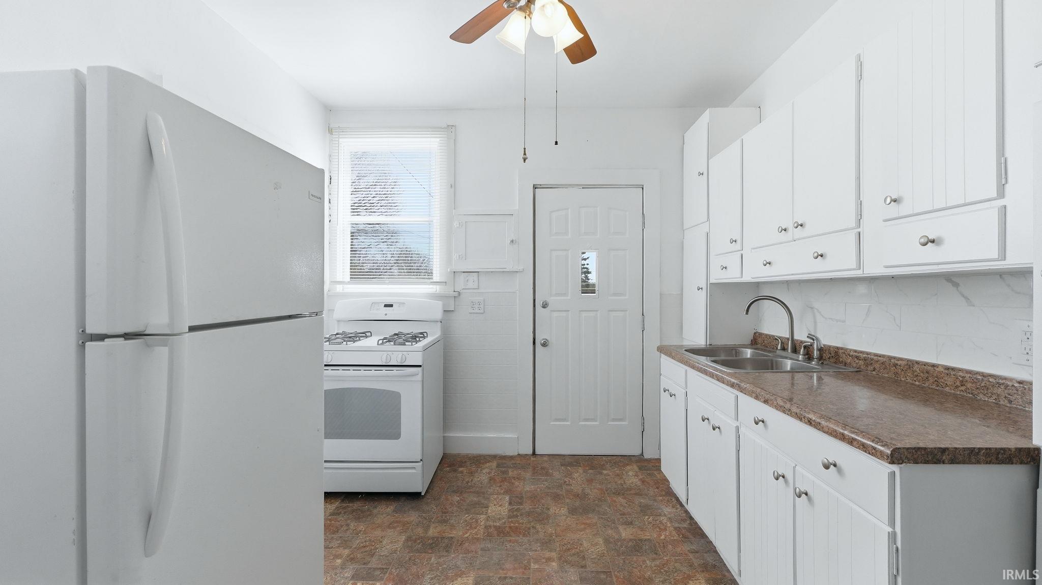 Kitchen featuring white appliances, stone finish flooring, white cabinets, dark countertops, and ceiling fan
