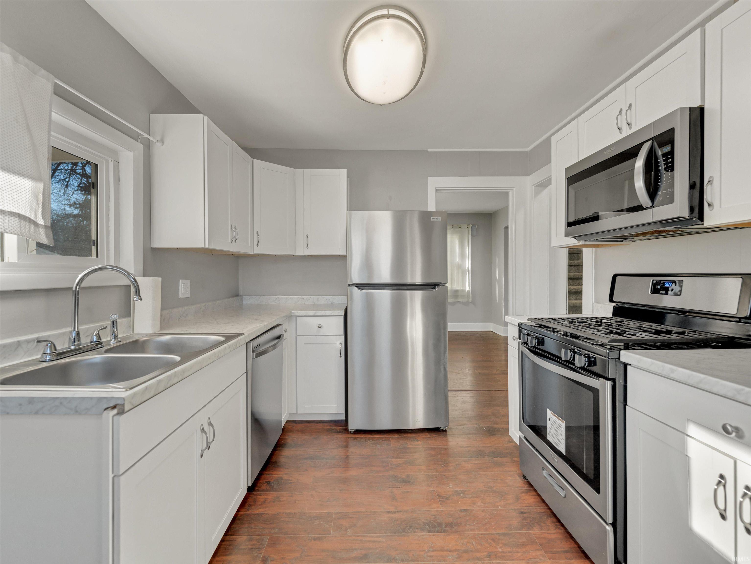 Kitchen featuring stainless steel appliances, healthy amount of natural light, light countertops, and dark wood-style floors