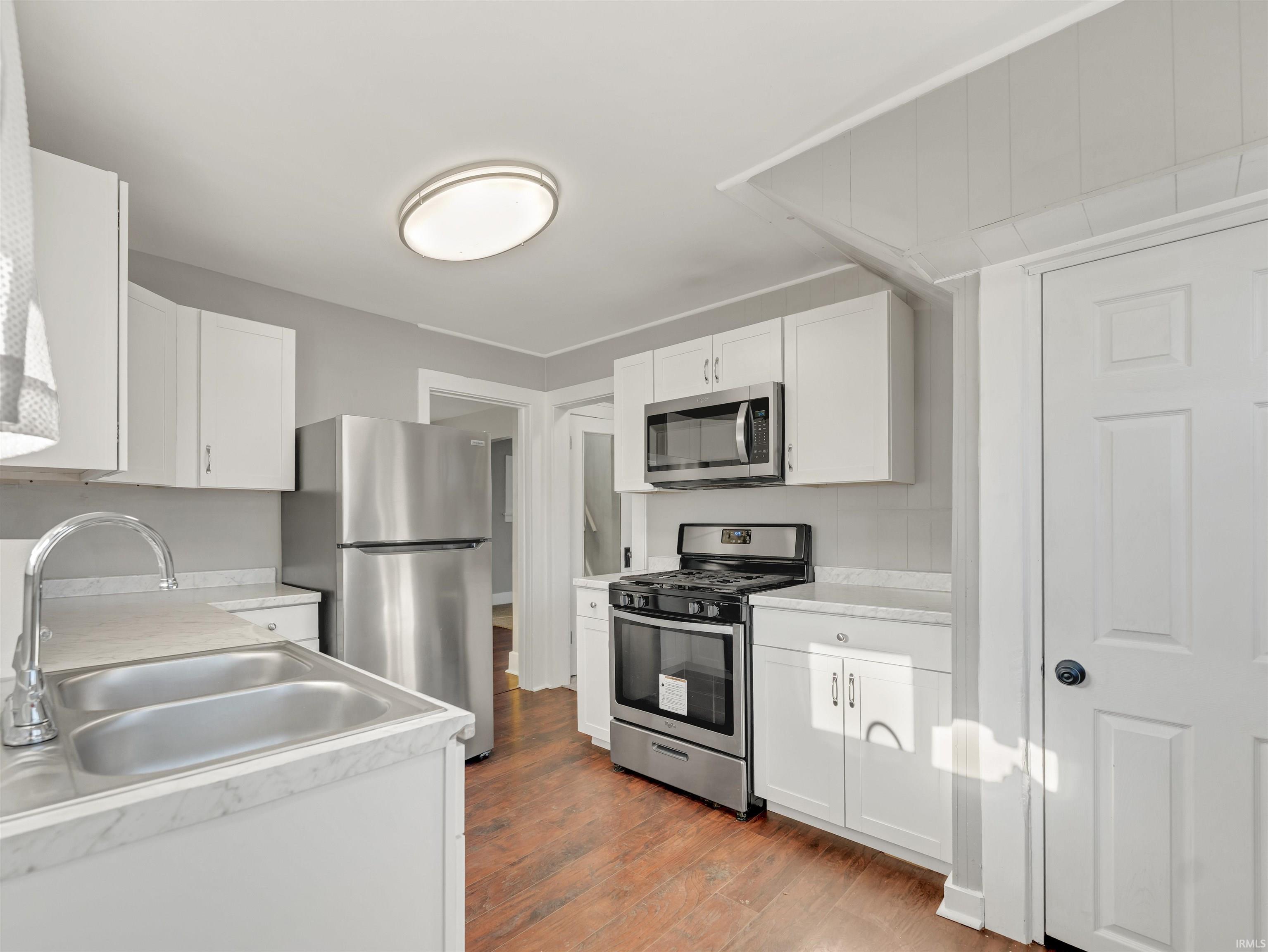 Kitchen featuring stainless steel appliances, white cabinetry, light wood-style floors, and light countertops