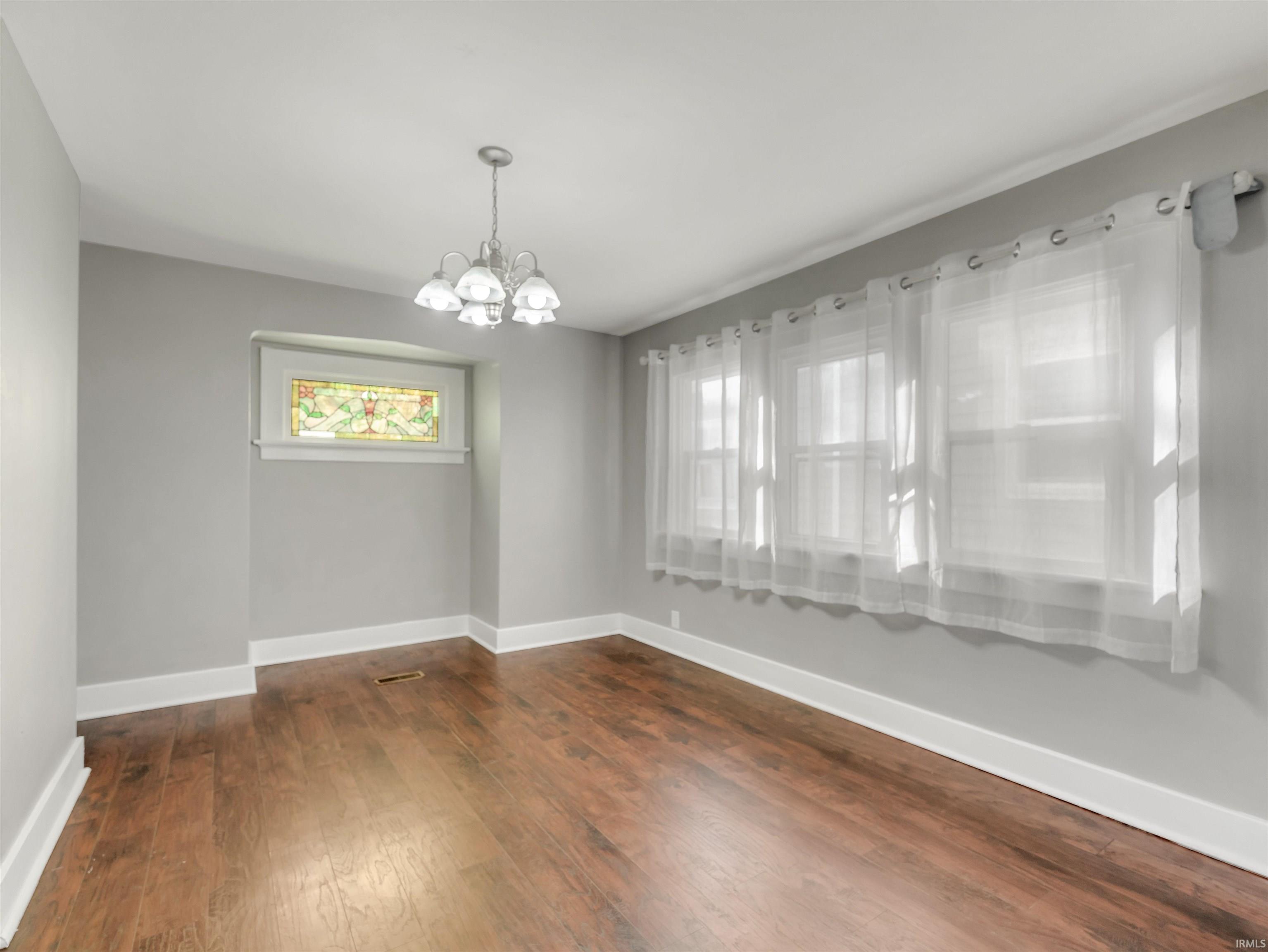 Spare room featuring suspended lighting and dark wood finished floors