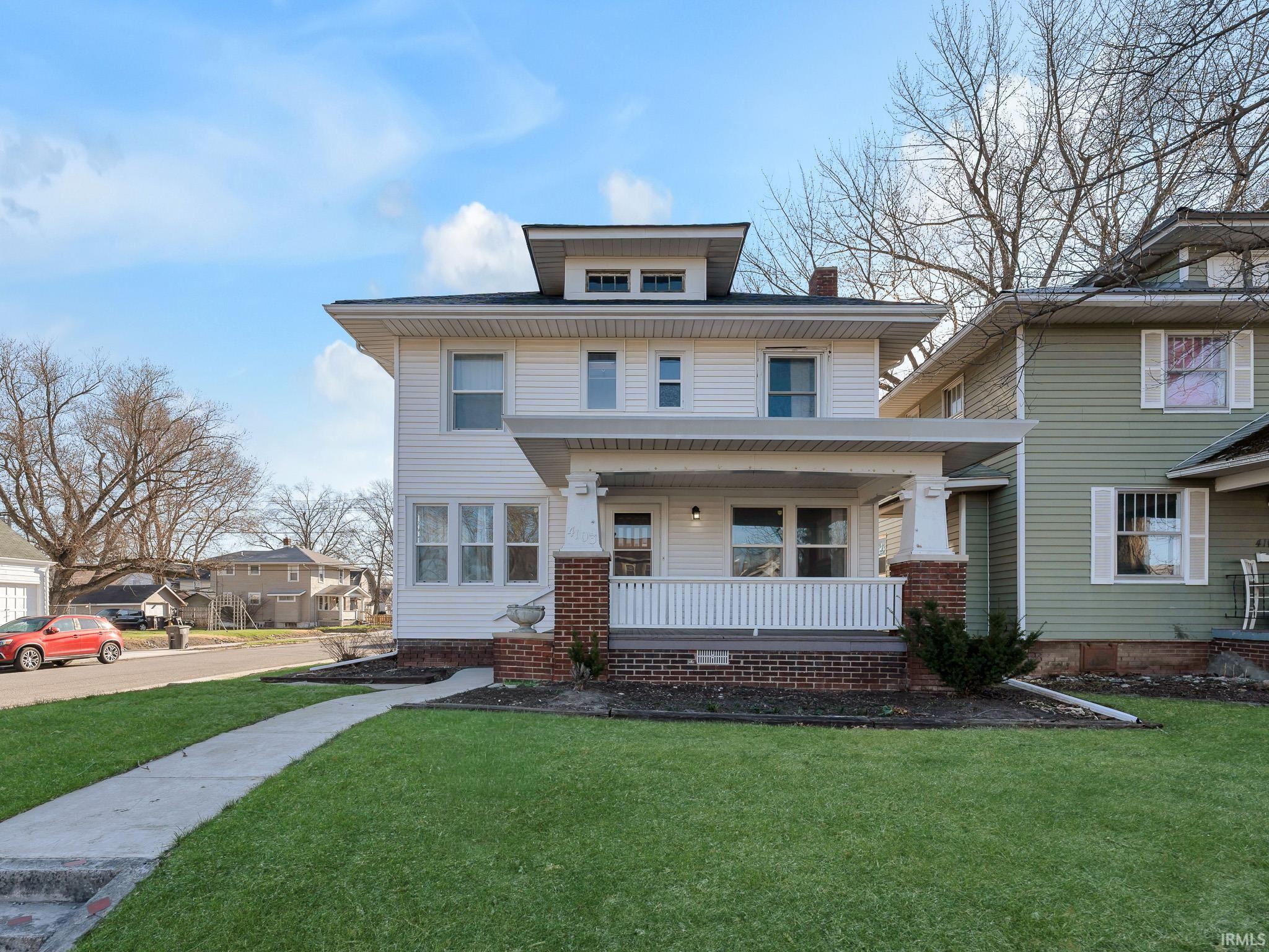 American foursquare style home with a porch, a front lawn, and a chimney
