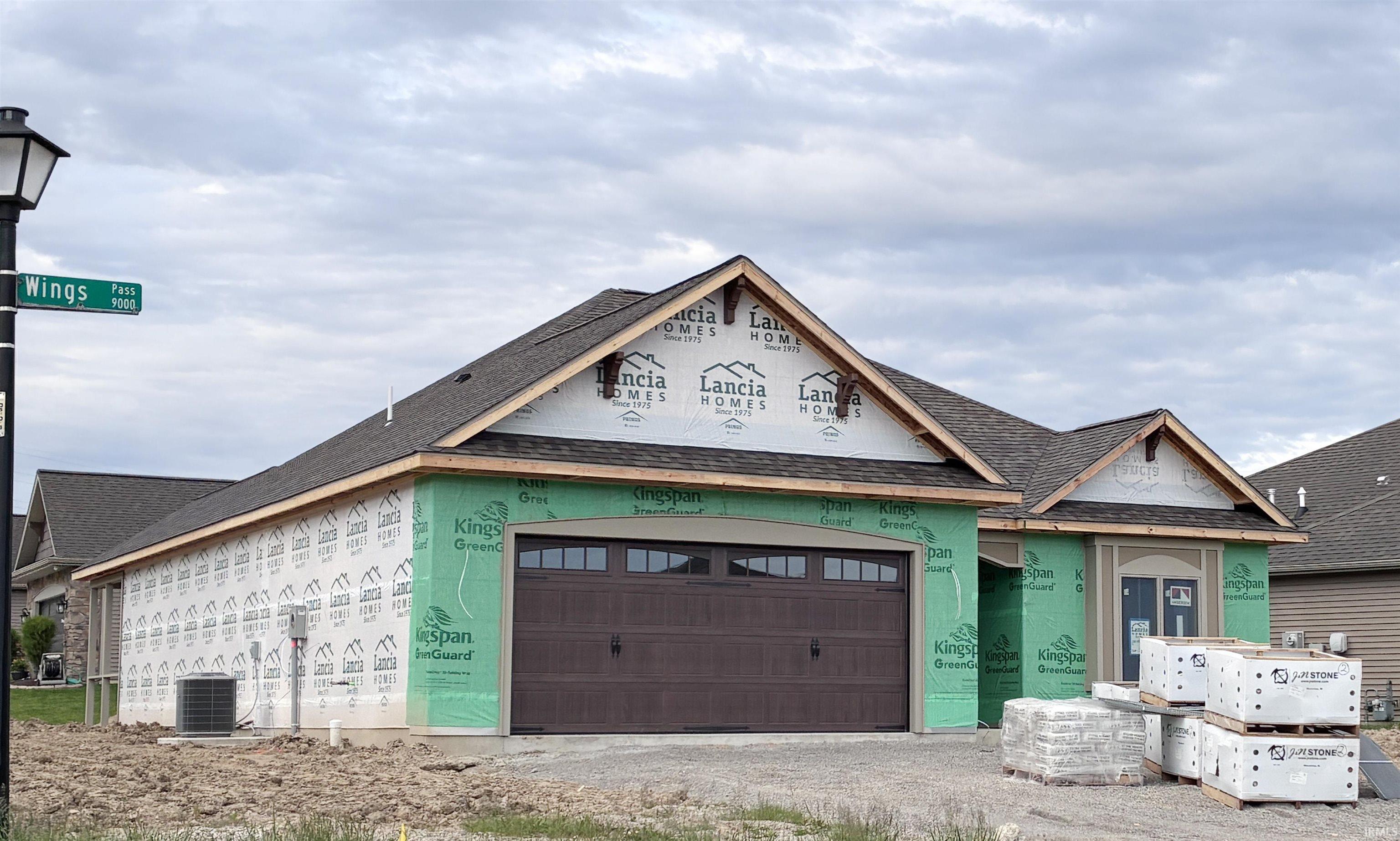 New construction home featuring a dark brown garage door with upper window inserts, an air conditioning unit, and partial exterior wrapping