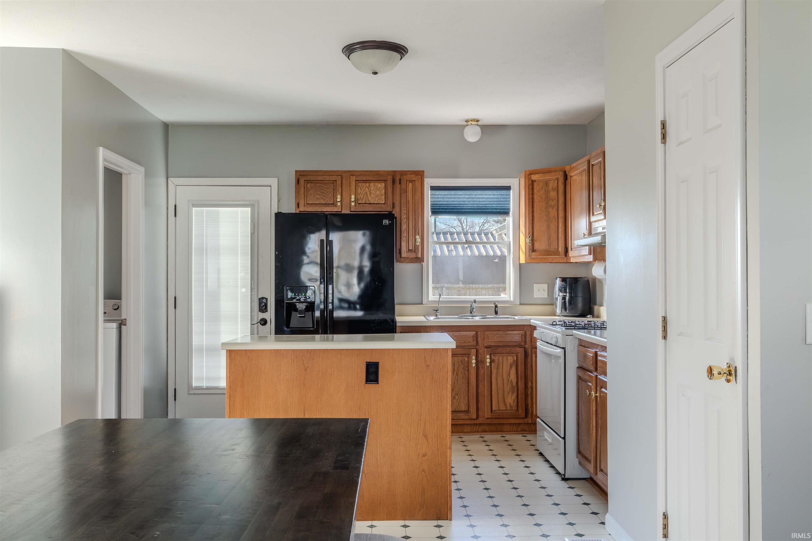 Kitchen featuring wood finish cabinets, black refrigerator with ice dispenser, light countertops, and white gas range