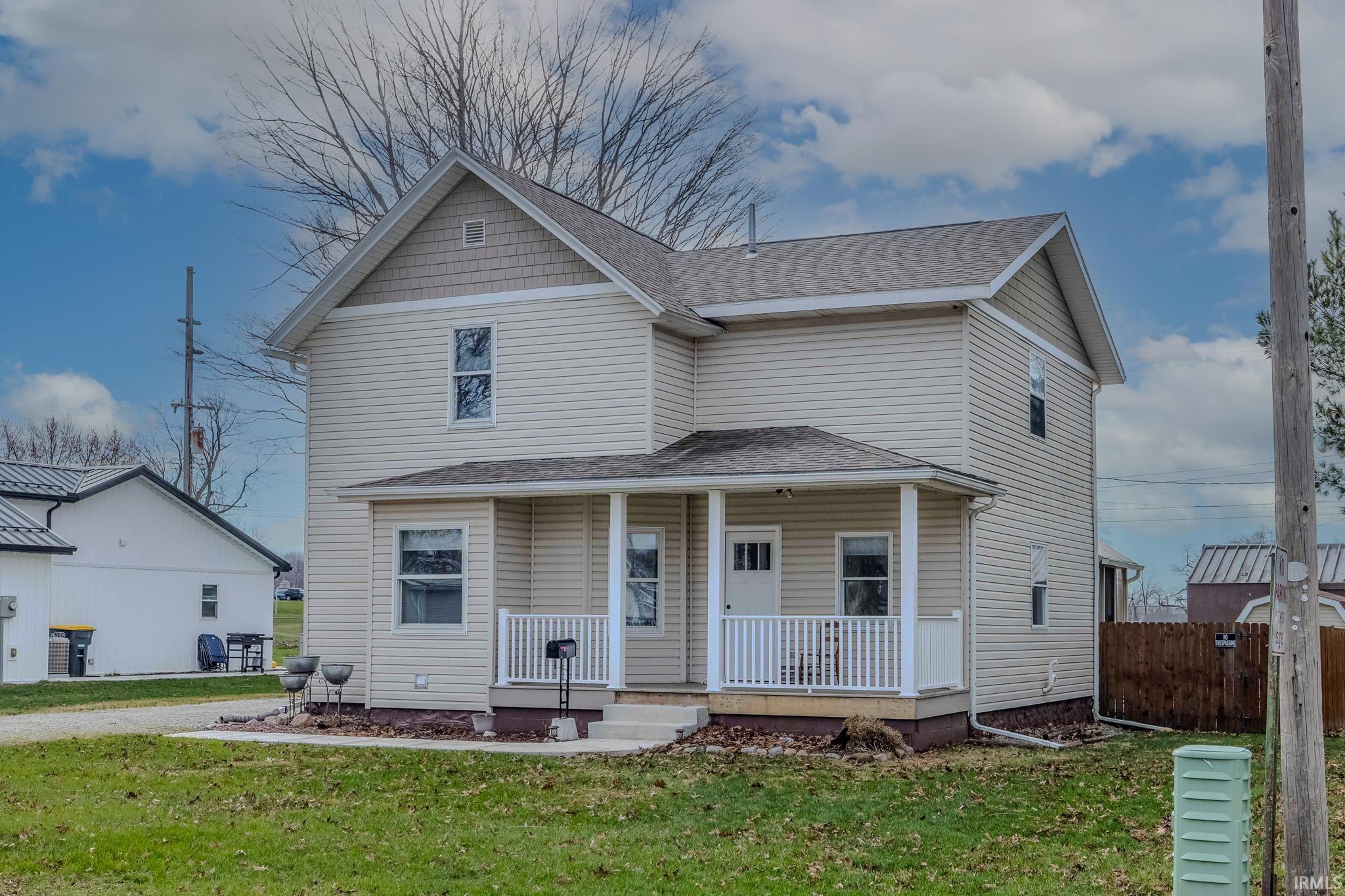 View of front of house with covered porch, a front yard, and roof with shingles