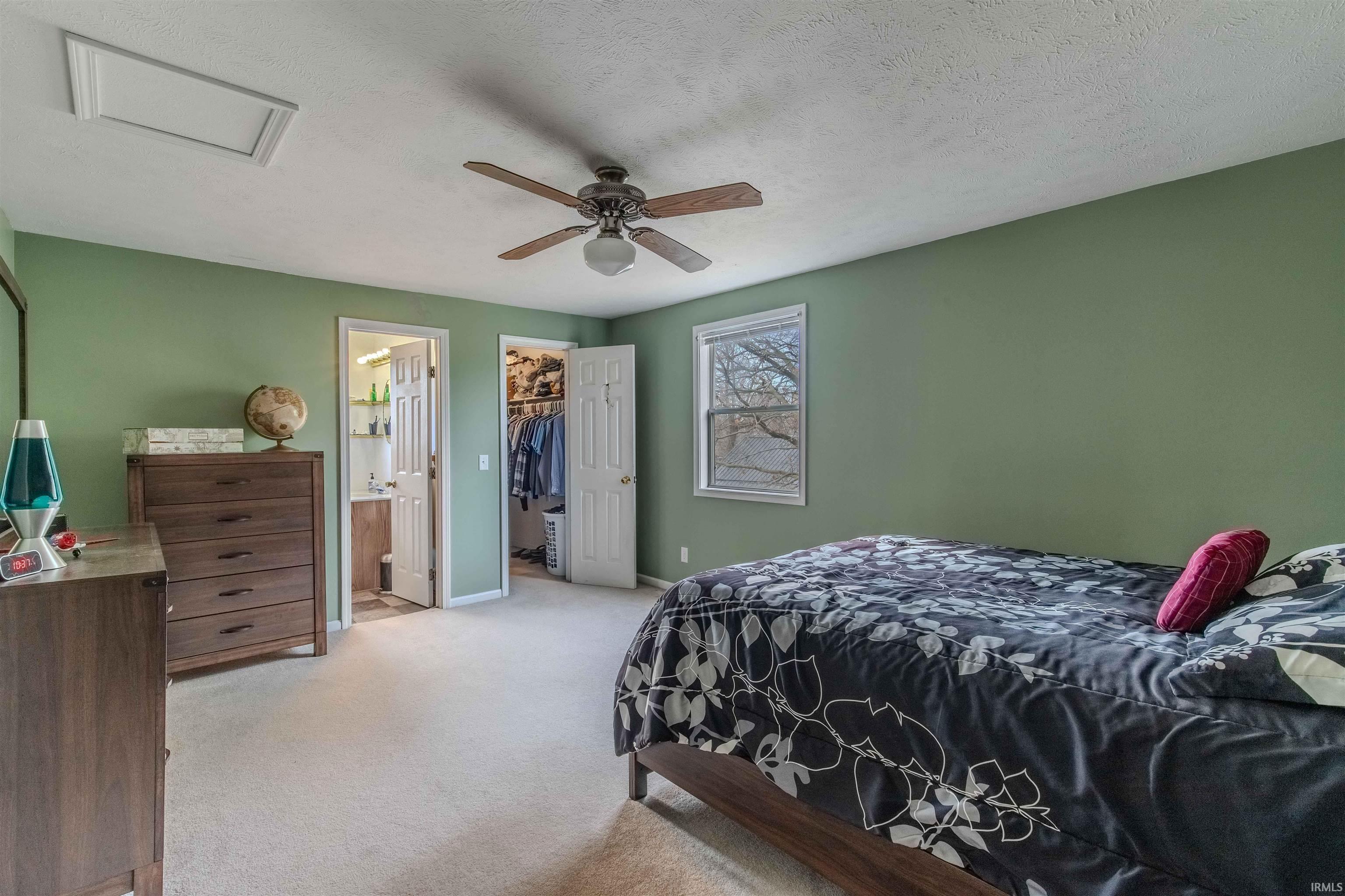 Bedroom featuring light carpet, a walk in closet, a textured ceiling, and a ceiling fan