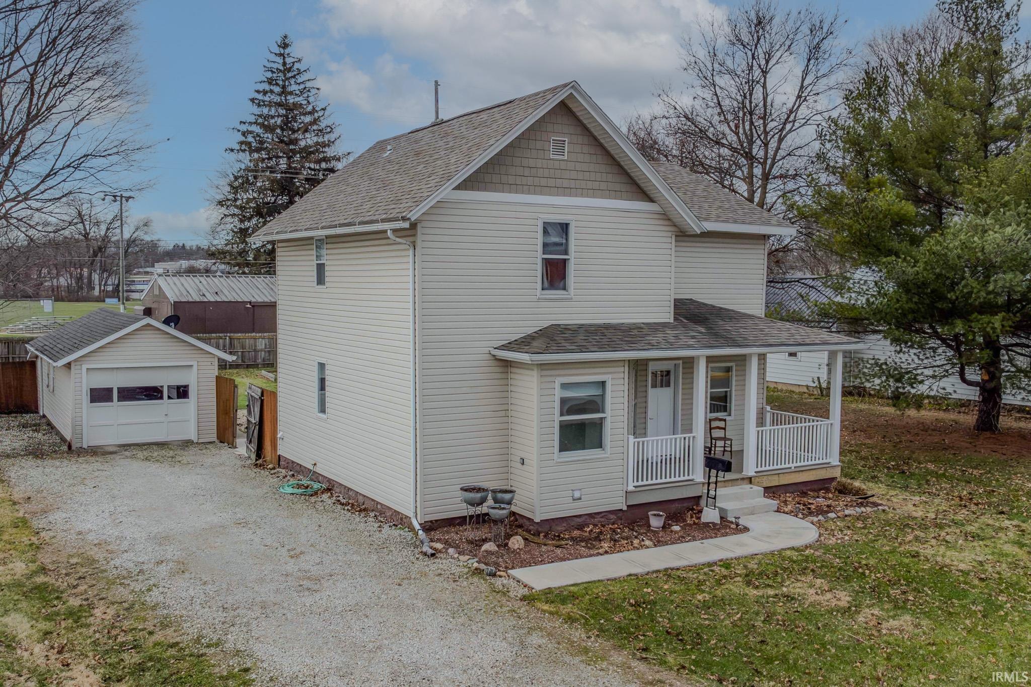 View of front of house featuring roof with shingles, covered porch, driveway, a garage, and an outbuilding