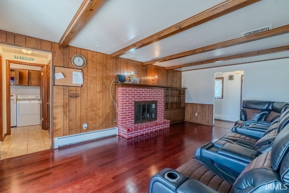 Living room with wooden walls, baseboard heating, wood finished floors, beam ceiling, and a fireplace