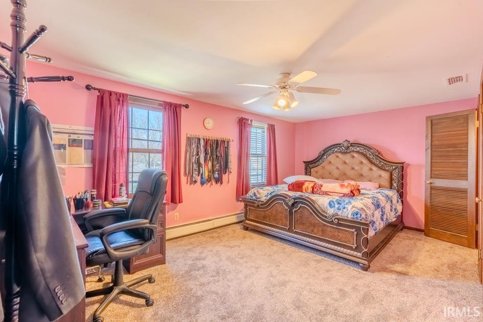 Bedroom with an office area, a baseboard radiator, a ceiling fan, and light colored carpet