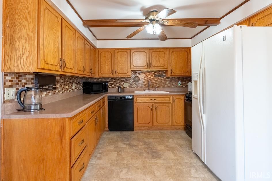 Kitchen featuring black appliances, light countertops, ceiling fan, stone finish floors, and wood finish cabinetry