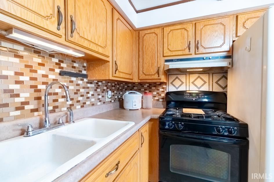Kitchen with black range with gas stovetop, decorative backsplash, light countertops, and light wood finish cabinets
