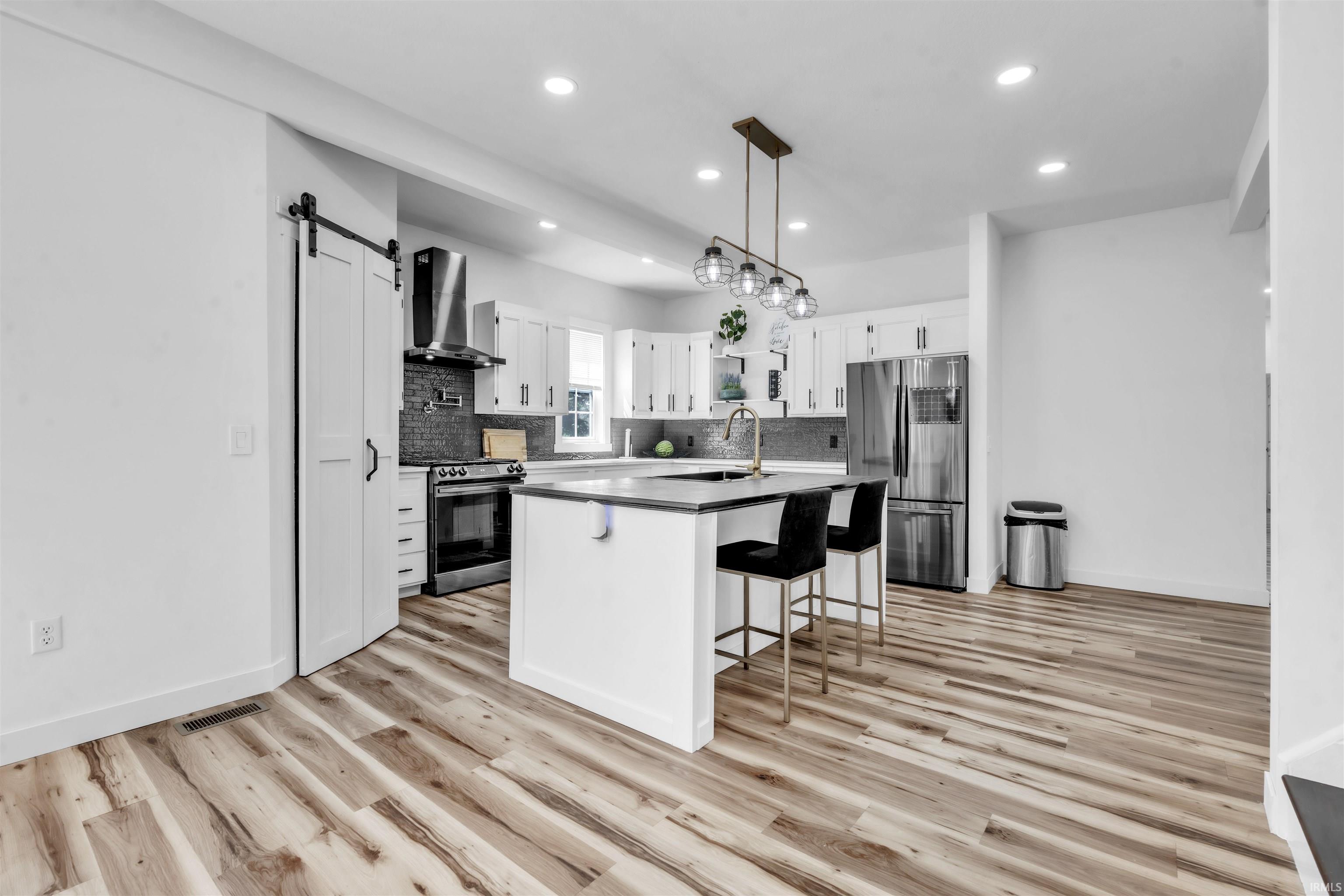 Kitchen featuring a barn door, a breakfast bar, white cabinets, and an island with sink