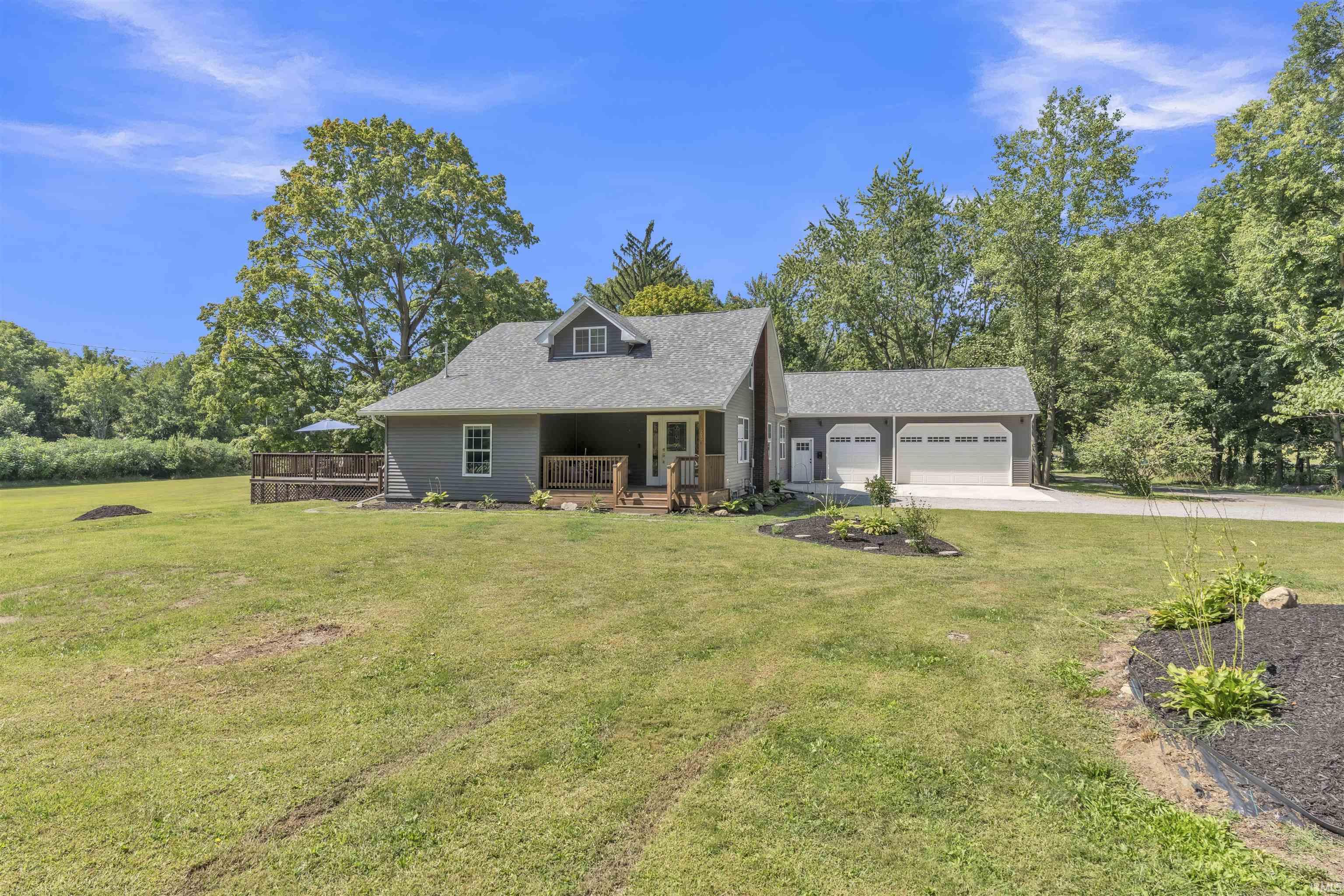 View of front facade with a porch, a front lawn, a garage, driveway, and view of wooded area
