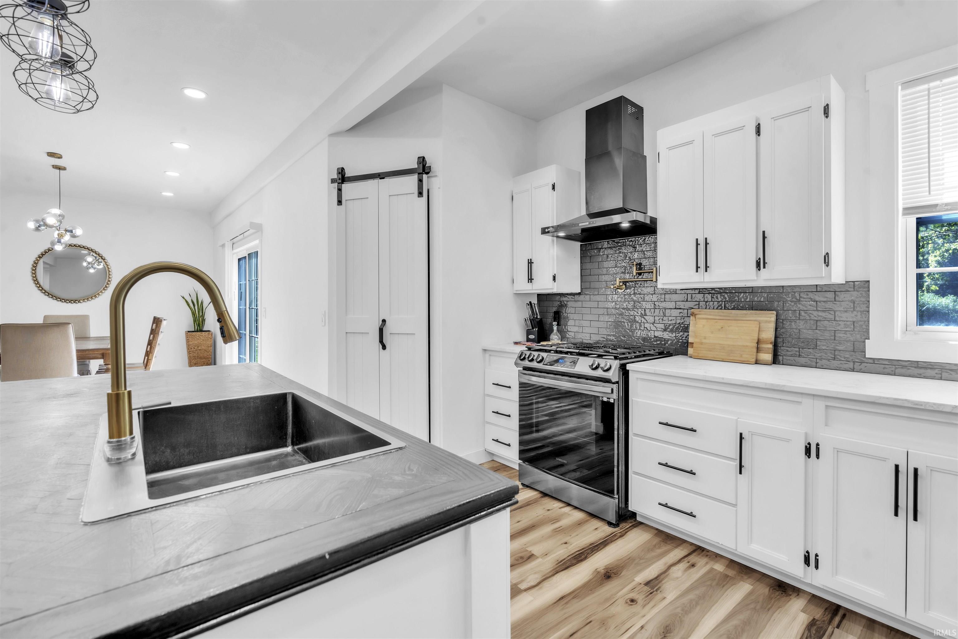 Kitchen with white cabinets, a barn door, stainless steel range with gas stovetop, and a chandelier