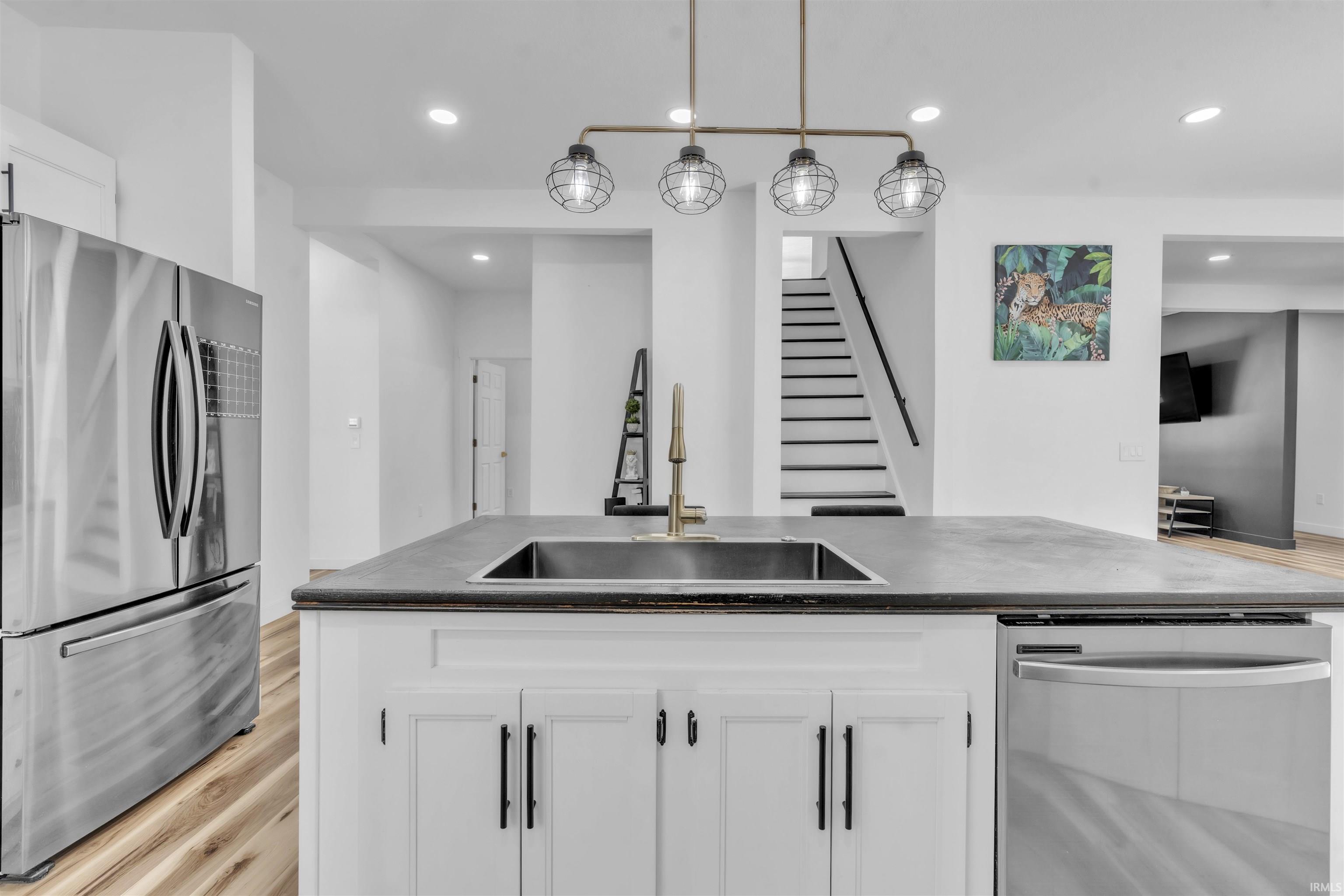 Kitchen featuring stainless steel appliances, white cabinets, light wood finished floors, and decorative light fixtures