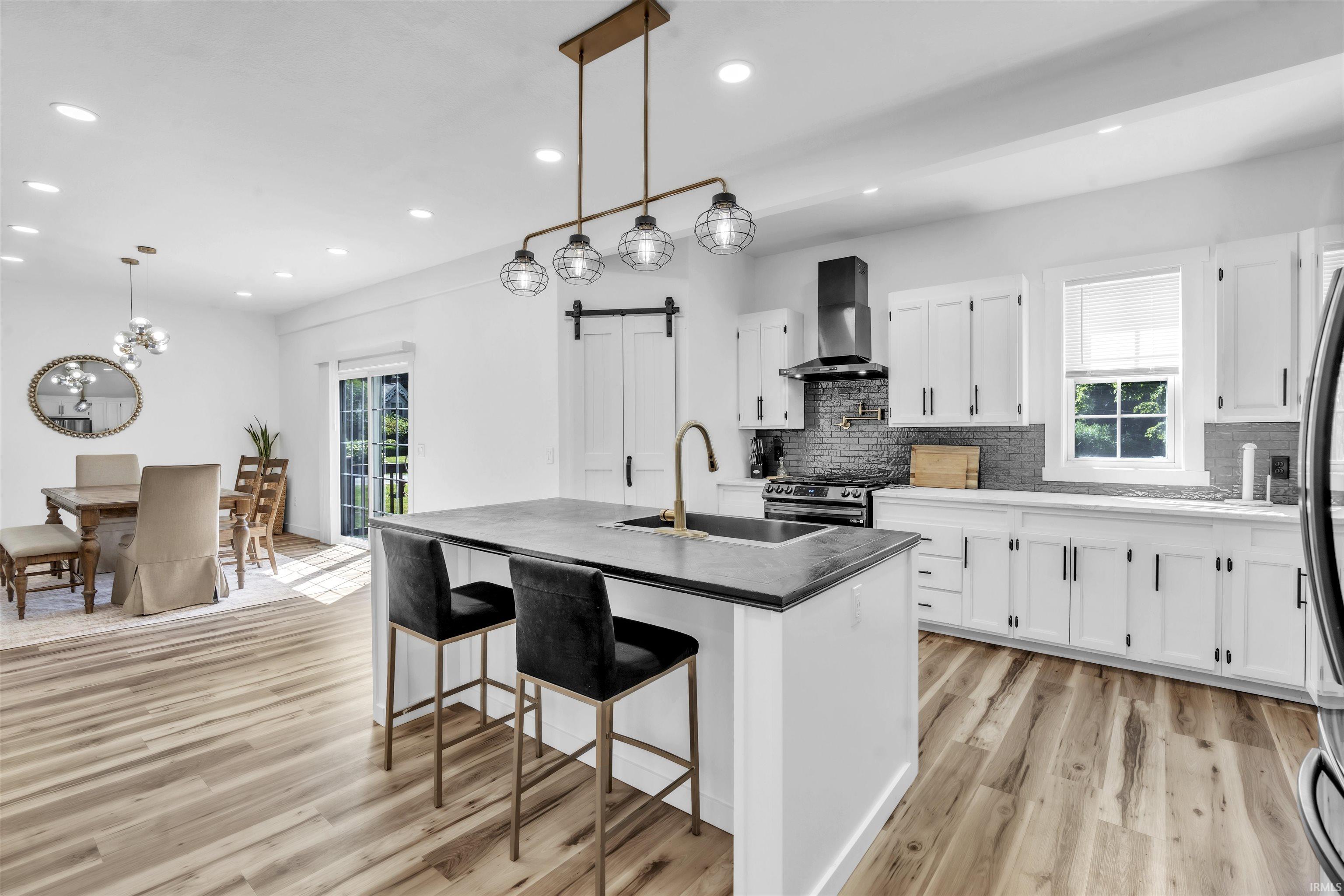 Kitchen featuring a barn door, a center island with sink, a kitchen breakfast bar, white cabinets, and light wood finished floors