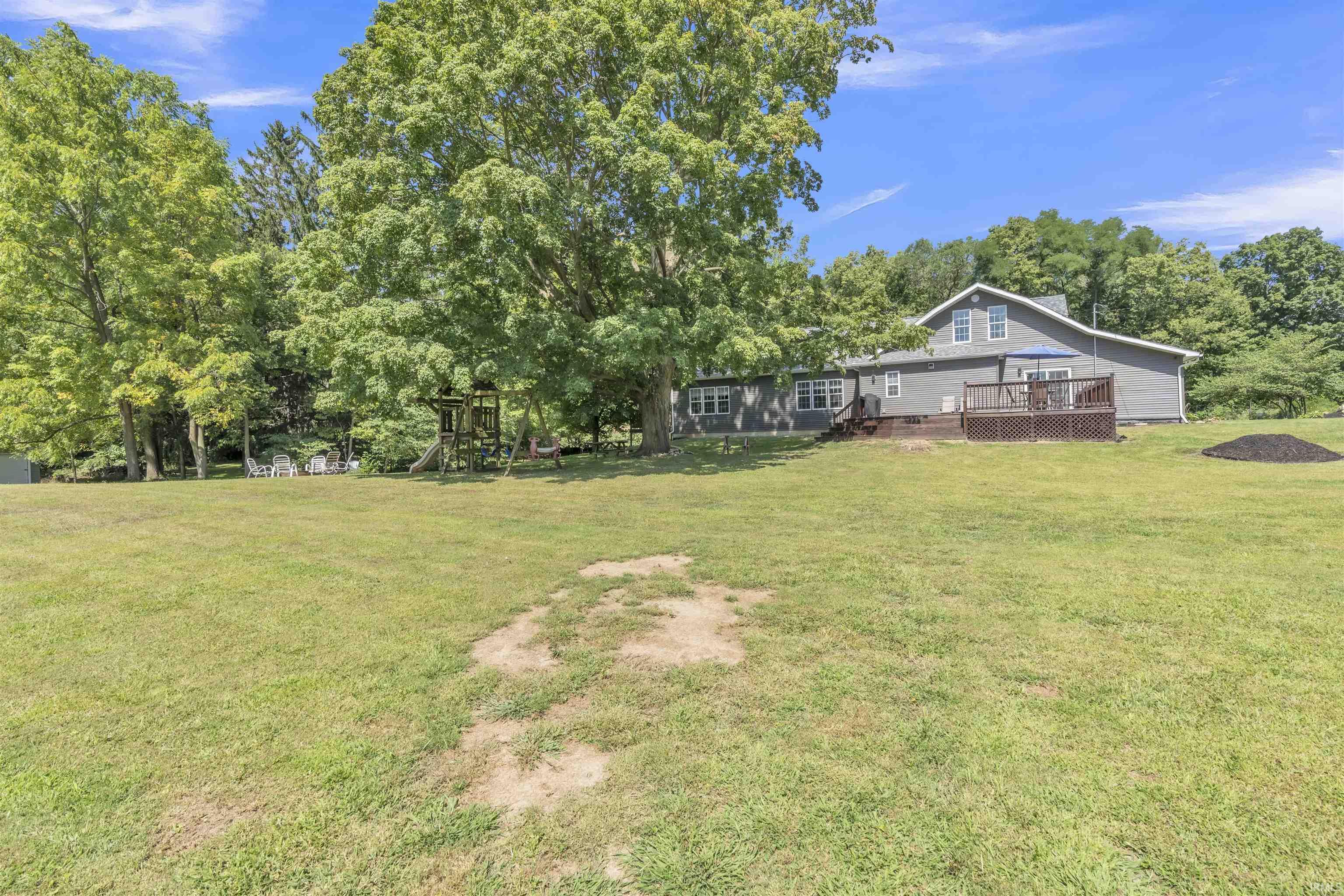 View of grassy yard featuring a wooden deck, a playground, and view of wooded area