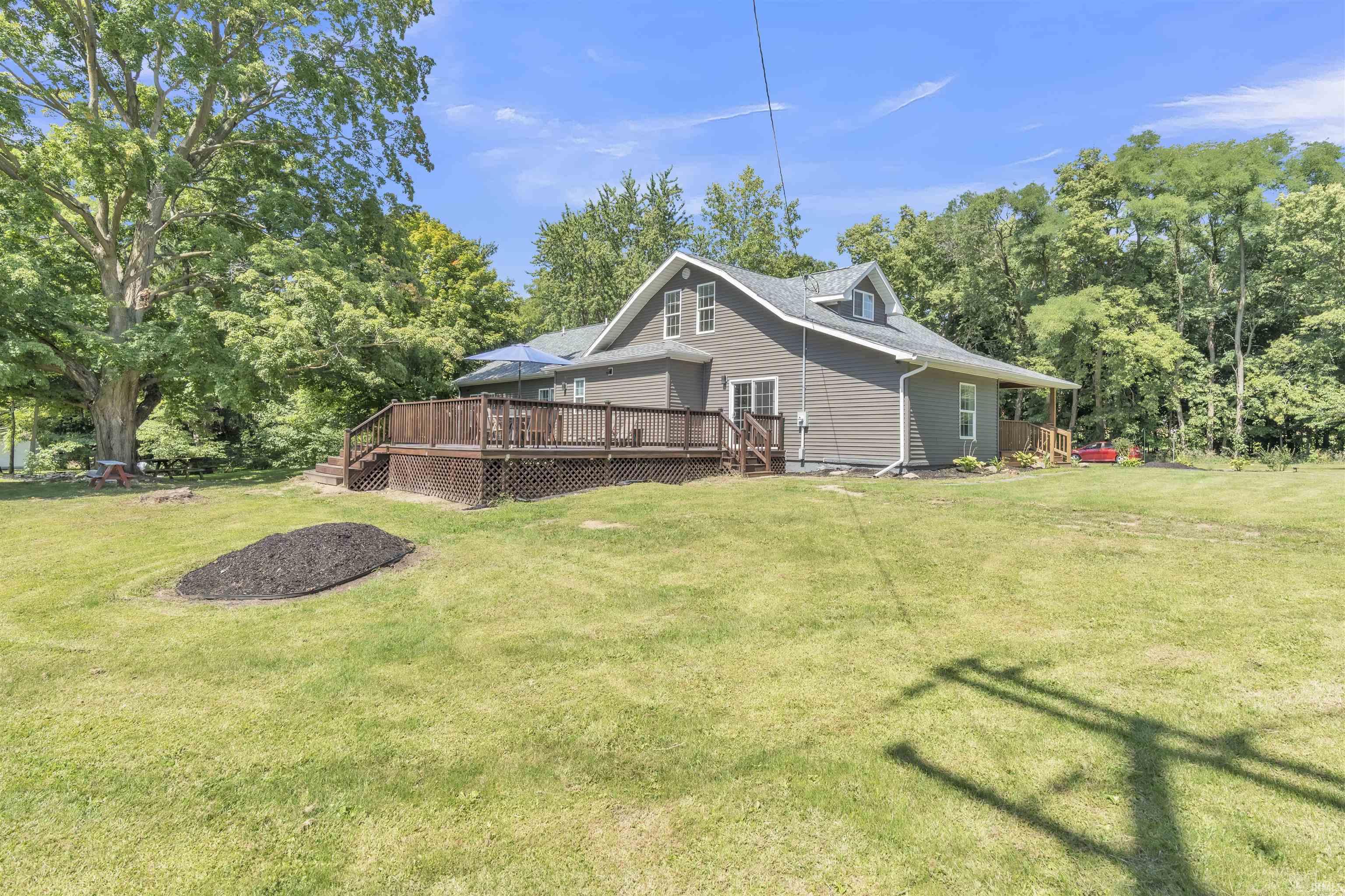 Back of house featuring a wooden deck, a lawn, and view of scattered trees