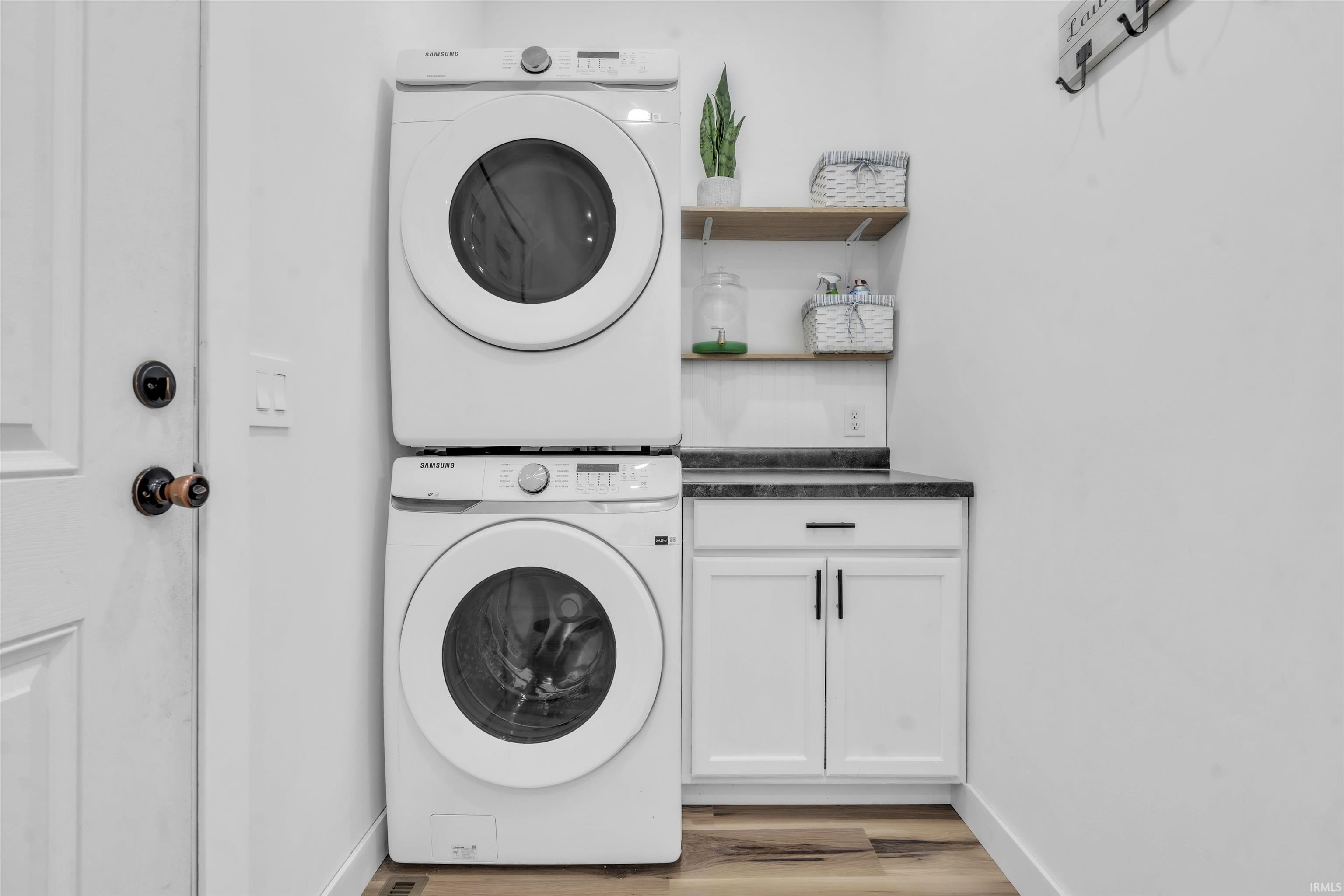 Laundry area featuring stacked washer / drying machine, light wood finished floors, and cabinet space