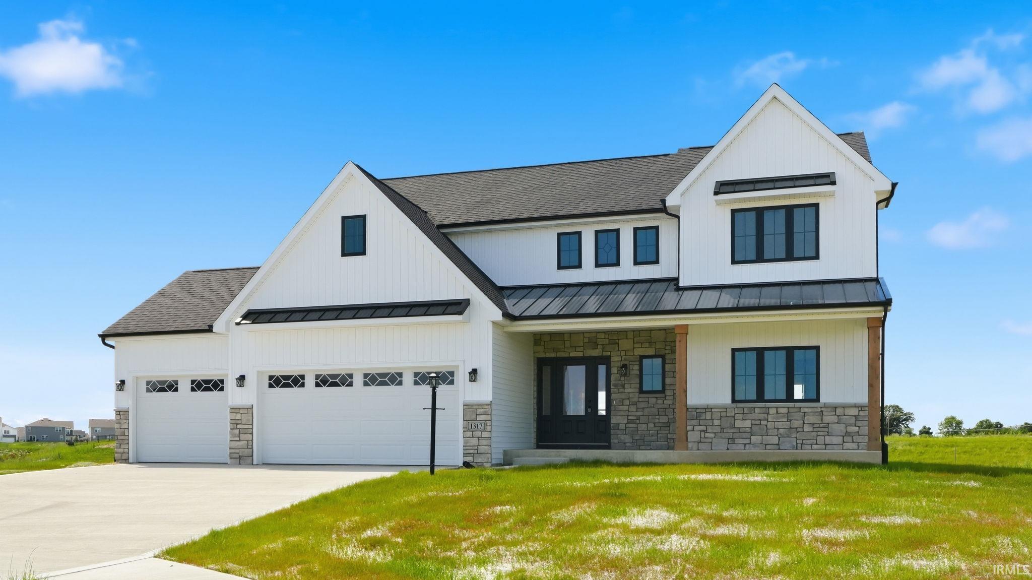 Modern farmhouse exterior featuring white board-and-batten siding, stone veneer accents, a dark shingled roof, black-framed windows, and a three-car garage with decorative window inserts