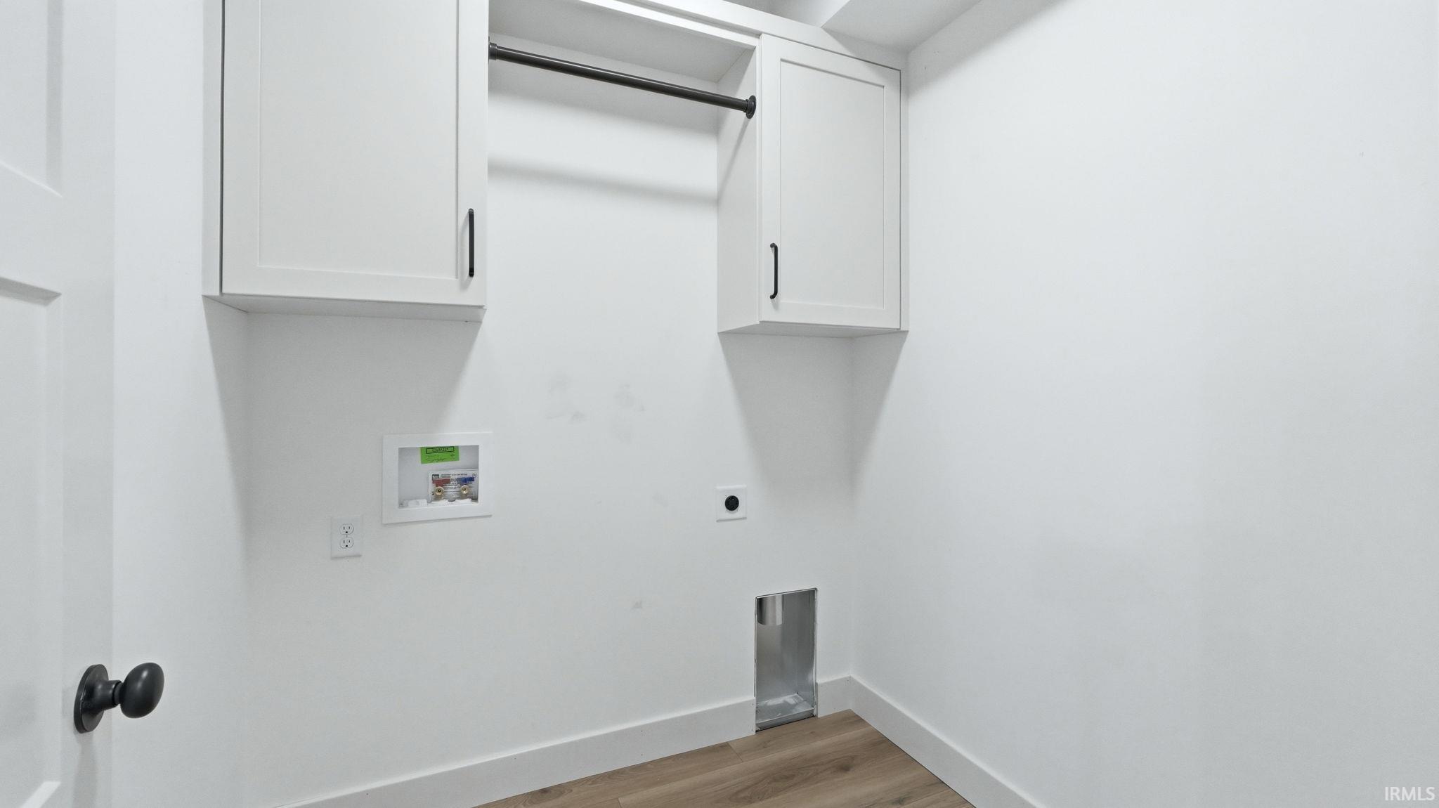 Dedicated laundry space featuring white shaker-style cabinetry with matte black hardware, a black hanging rod, and wood-finish flooring