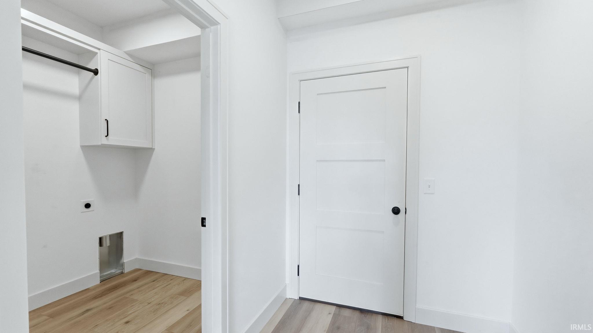 Laundry area featuring wood-finish flooring, white cabinetry with black hardware, and a hanging rod