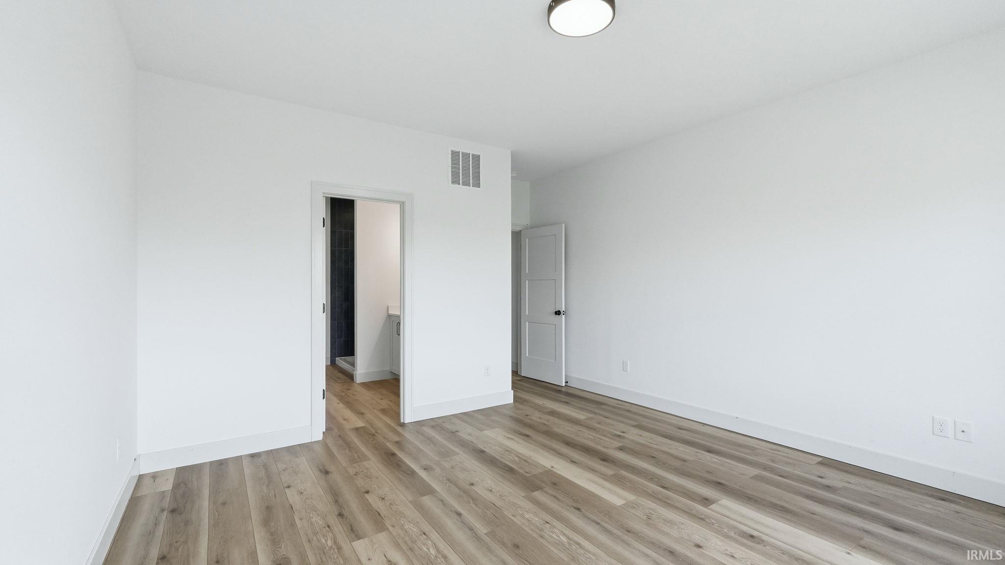 Spacious room featuring wood-finish flooring, white baseboards, and bright white walls
