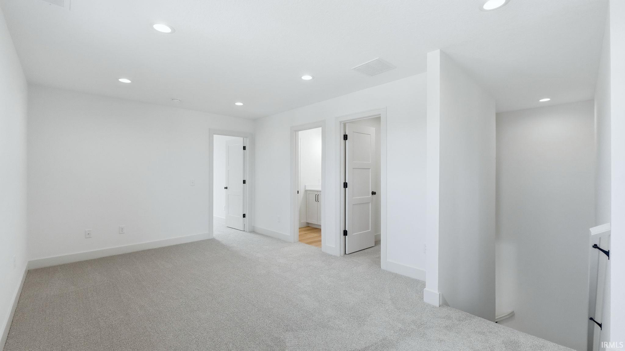 Spacious hallway featuring light gray carpeting, recessed ceiling lighting, crisp white walls, and white trim