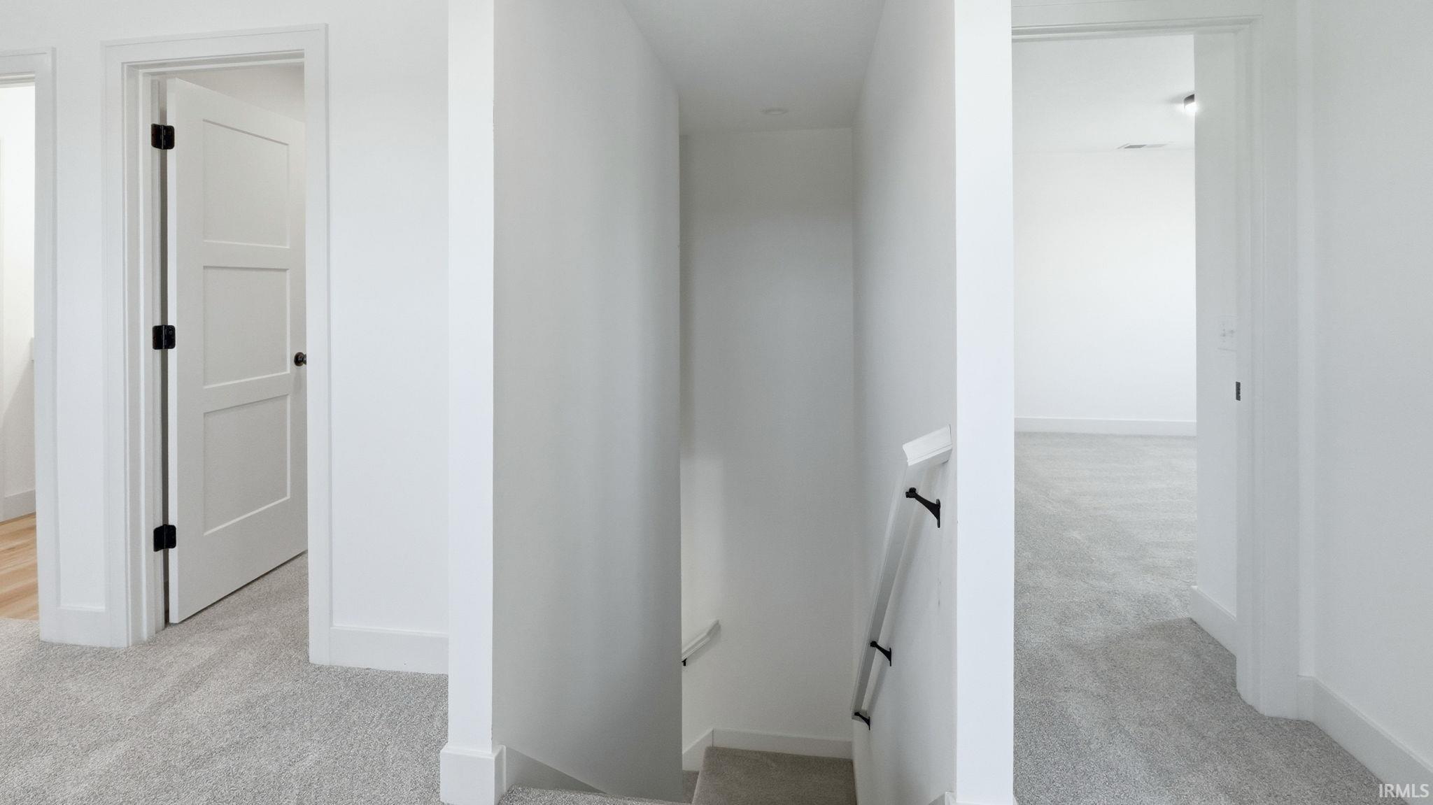 Hallway featuring light gray carpet, white walls, white baseboards, and a white three-panel door with black hardware