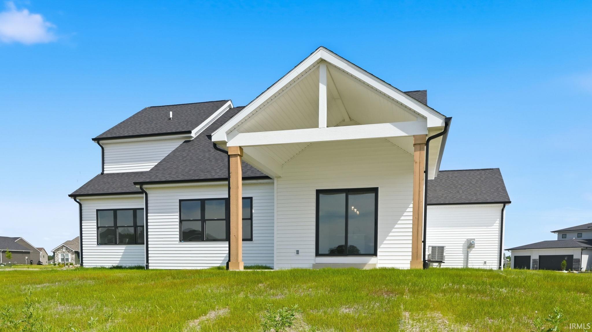 White siding exterior with a black shingle roof, featuring a covered patio with exposed wood columns and a vaulted ceiling