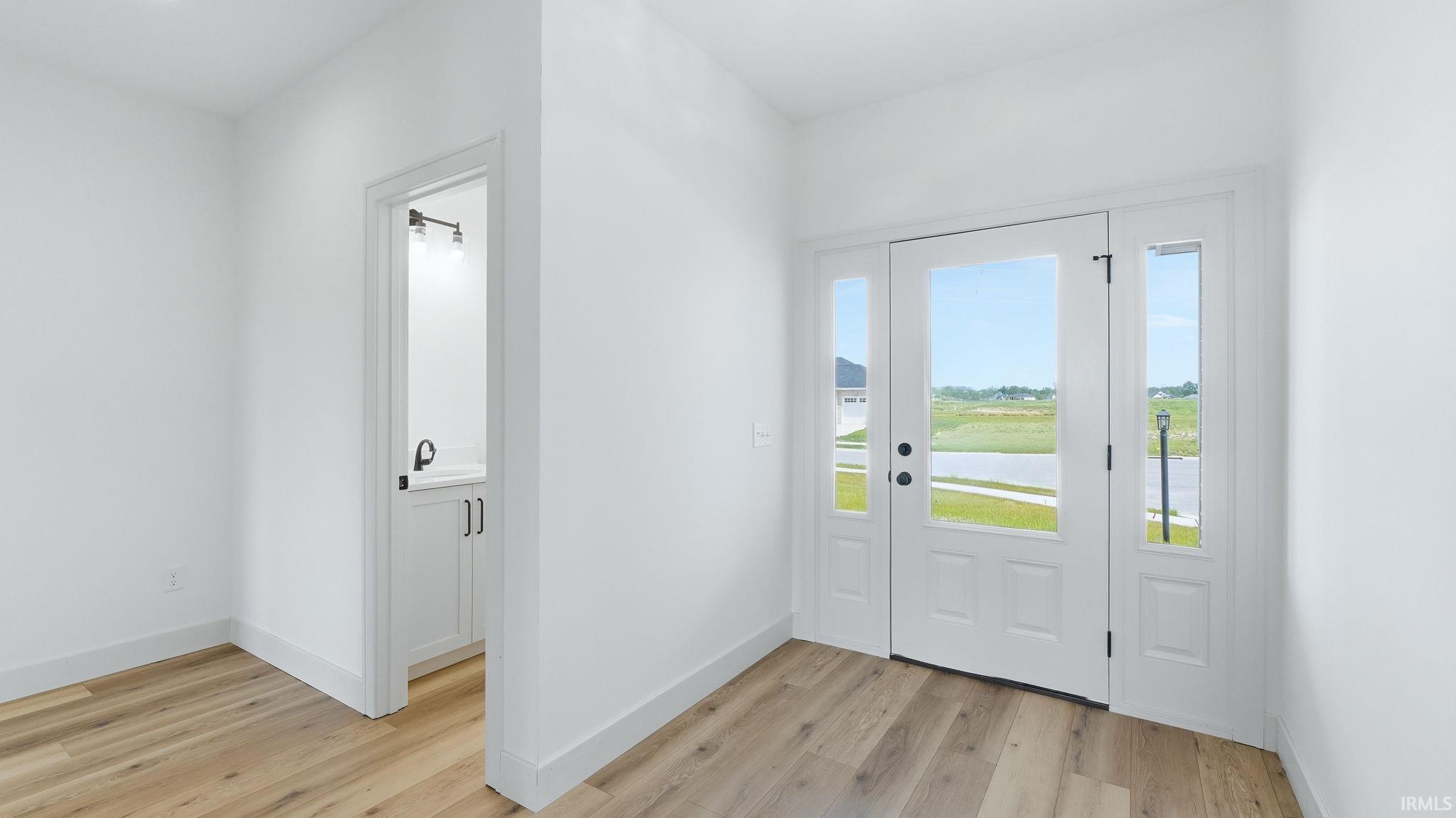 Entryway featuring wood-finish flooring, white baseboards, and a white paneled front door with clear glass inserts
