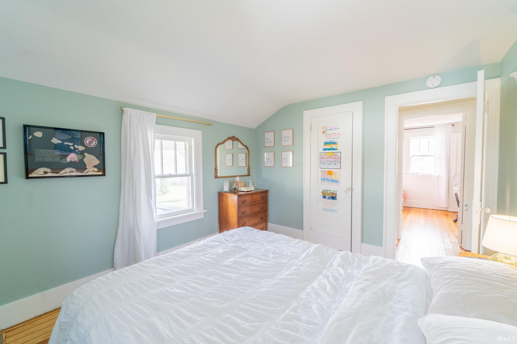 Bedroom featuring lofted ceiling, light wood-type flooring, and multiple windows