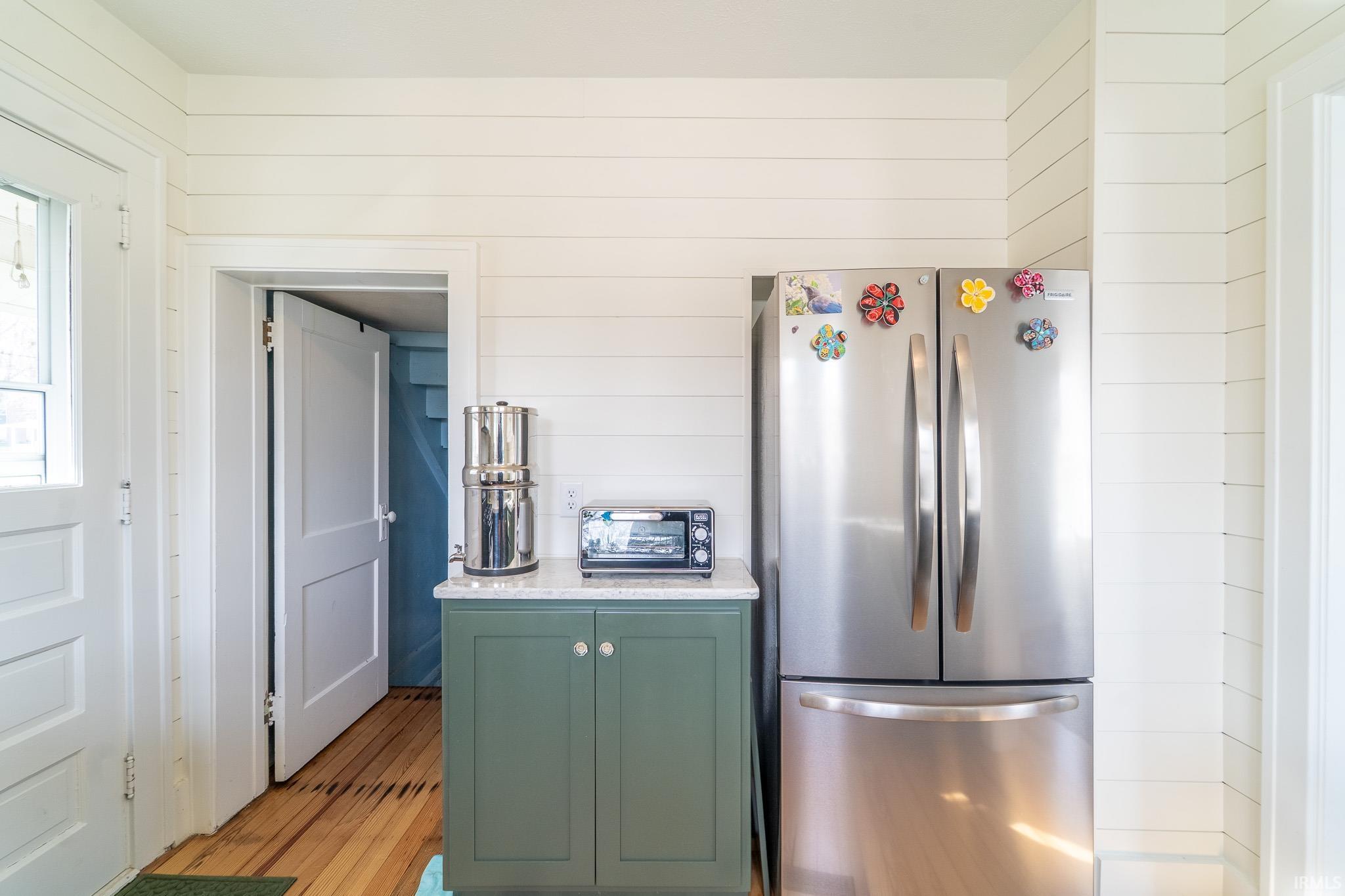 Kitchen featuring freestanding refrigerator, green cabinets, wood walls, light wood finished floors, and light stone countertops