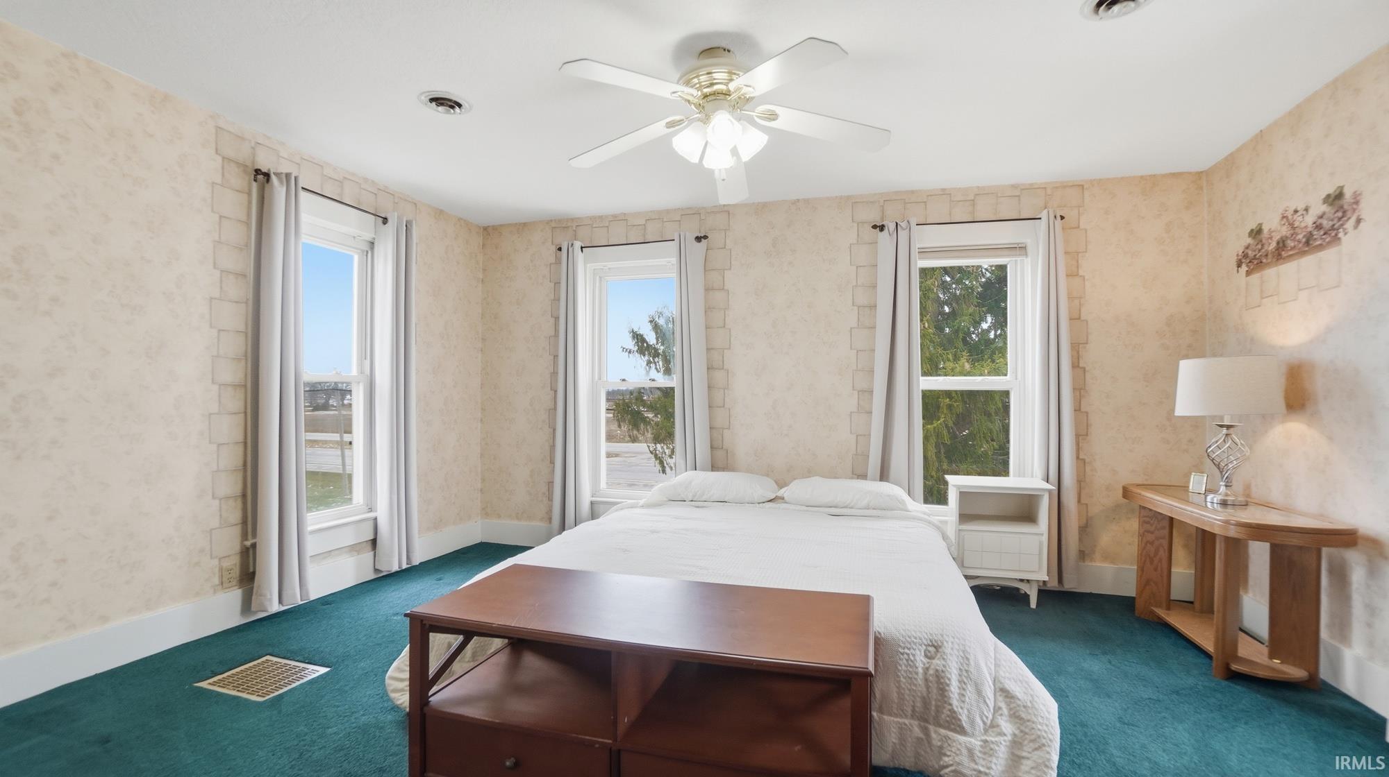 Carpeted bedroom with wallpapered walls and ceiling fan